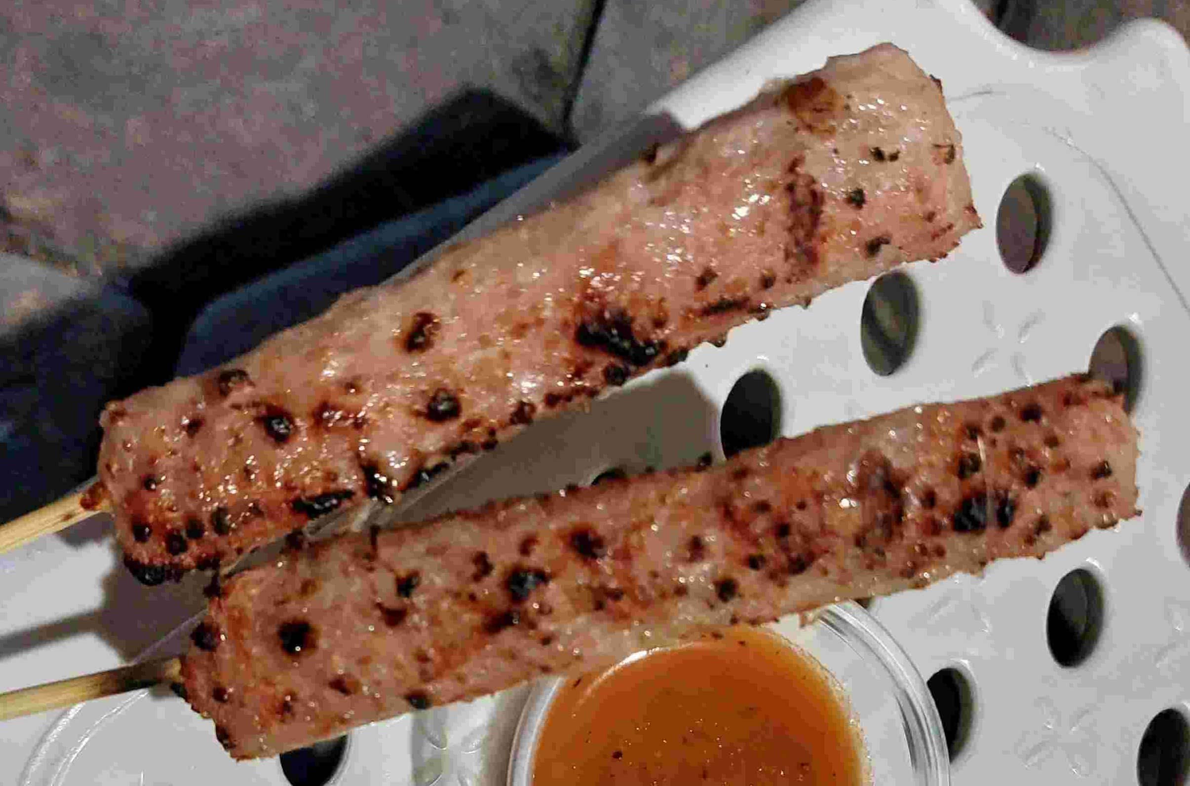 Nem nướng – Two grilled Vietnamese pork skewers served with a small bowl of chilli dipping sauce.