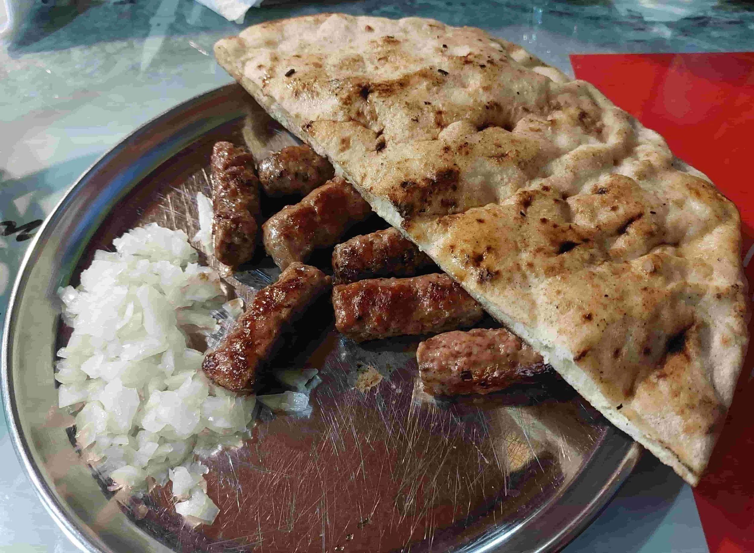 Close-up of Bosnian Ćevapi served with traditional lepinja bread, and fresh onions