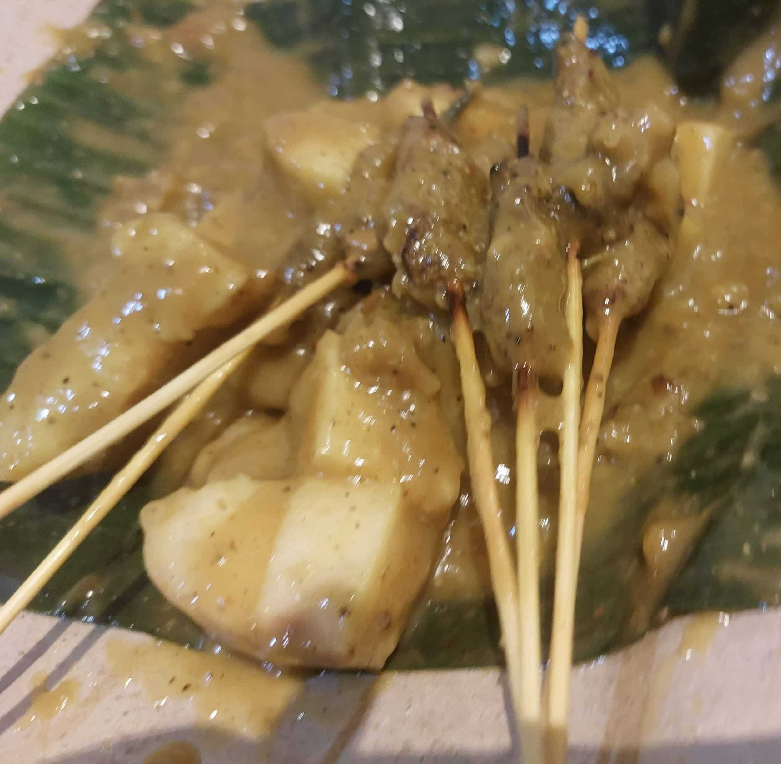 Sate Padang Indonesian beef skewers with thick spicy yellow sauce, served with lontong rice cakes on a banana leaf