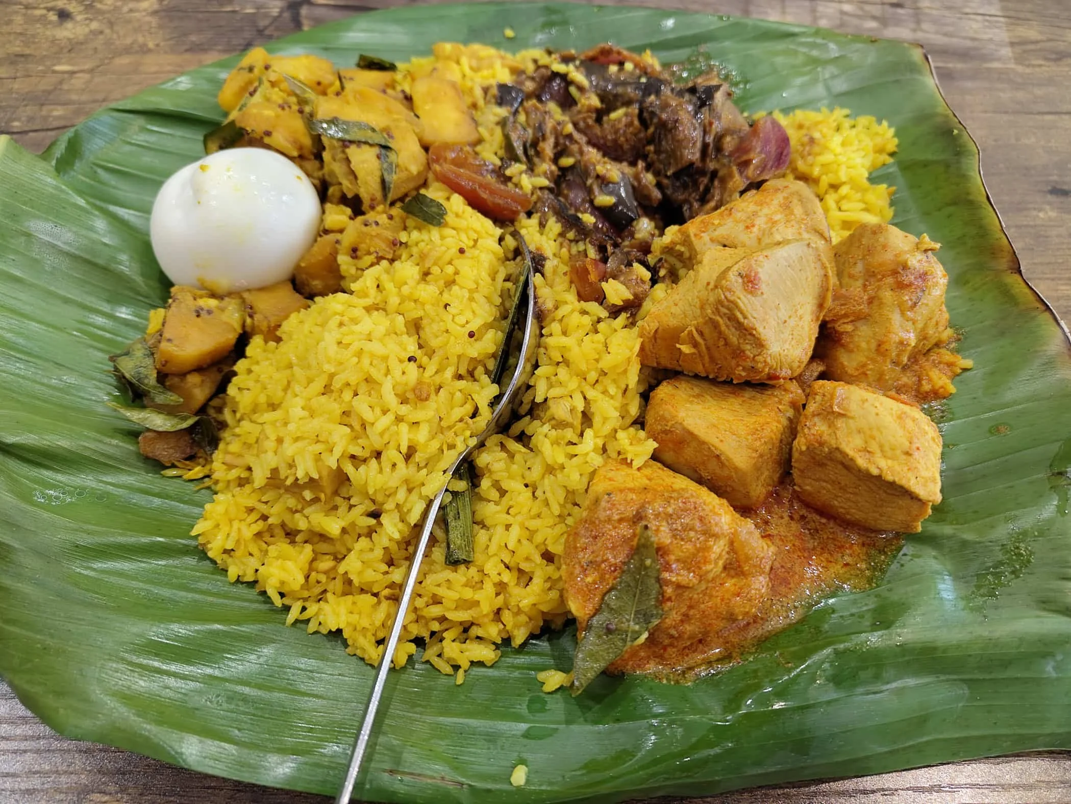 Sri Lankan lamprais served on a banana leaf with chicken curry, yellow rice, ash goud, wambatu moju and an egg