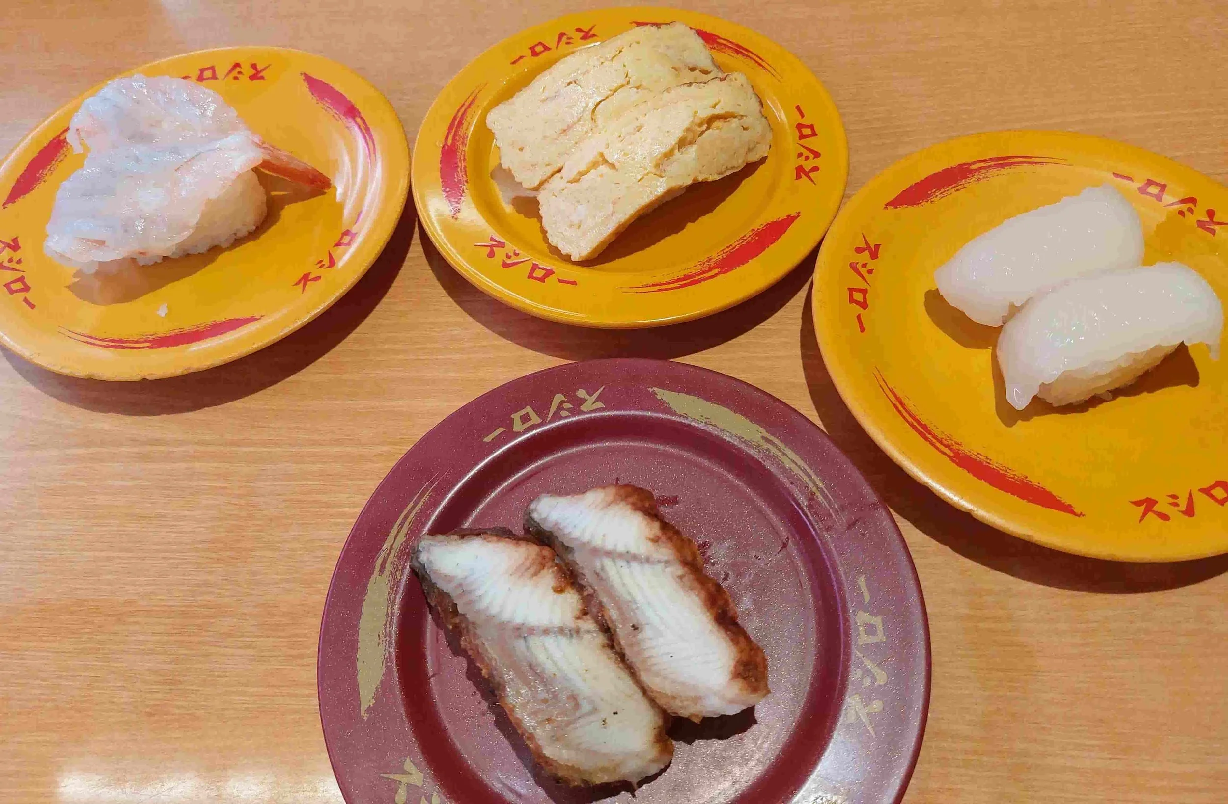 Four plates of nigiri sushi with tamago (egg), prawn, squid, and eel
