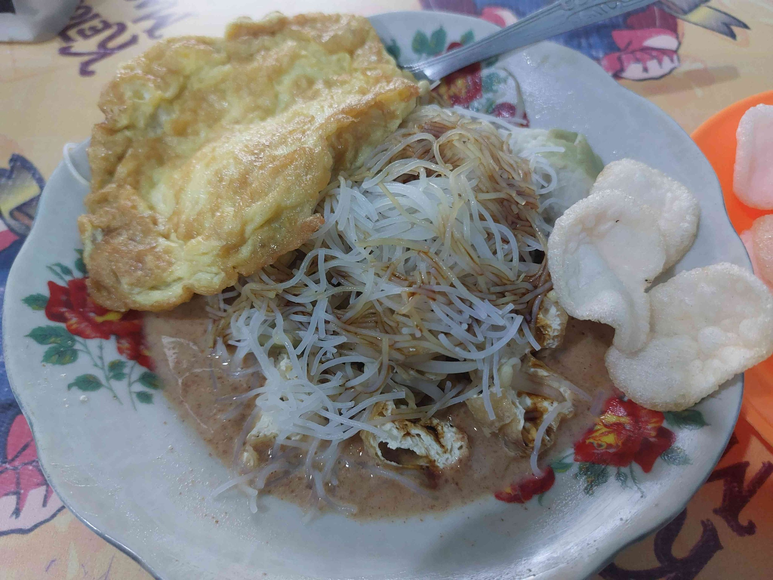 Indonesian Ketoprak with rice noodles, fried tofu, crispy crackers, and fried egg topped with peanut sauce