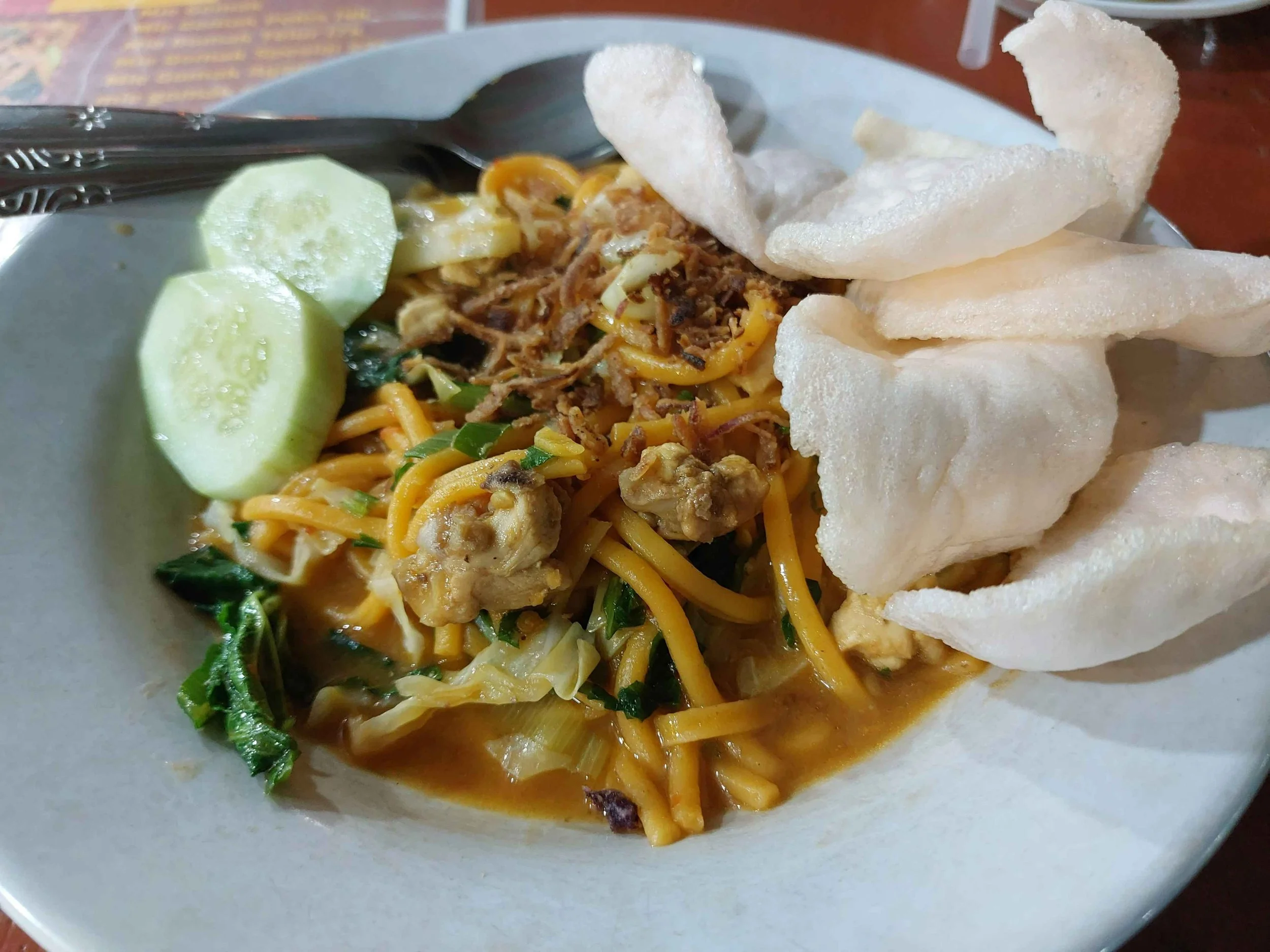 Traditional Batak mie gomak spicy noodles served with crackers and cucumber slices on the side