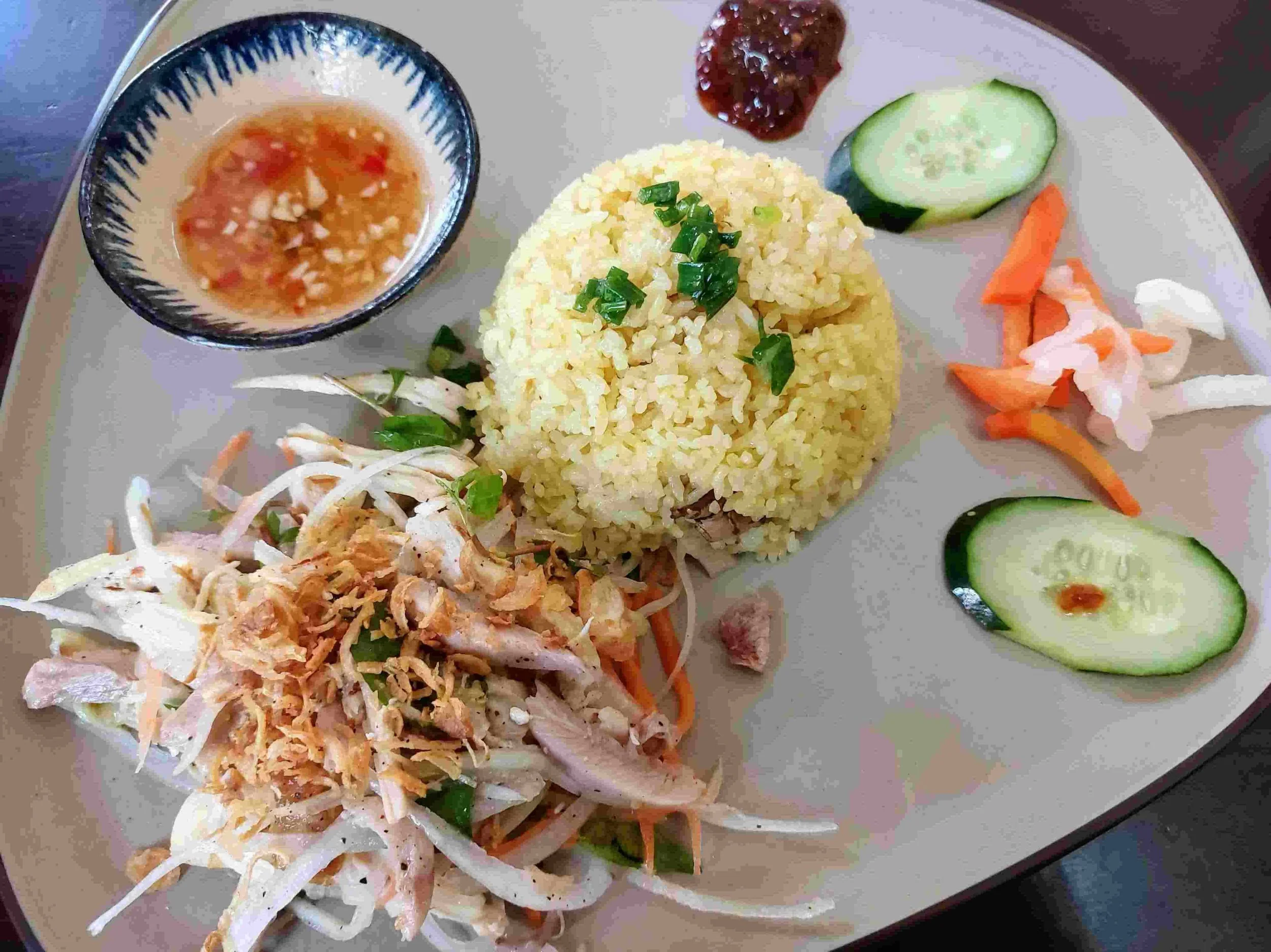 Cơm gà – Vietnamese chicken rice with shredded poached chicken, fragrant rice cooked in chicken broth, a fresh side salad of pickled vegetables and herbs, and a small dish of traditional nước chấm dipping sauce.