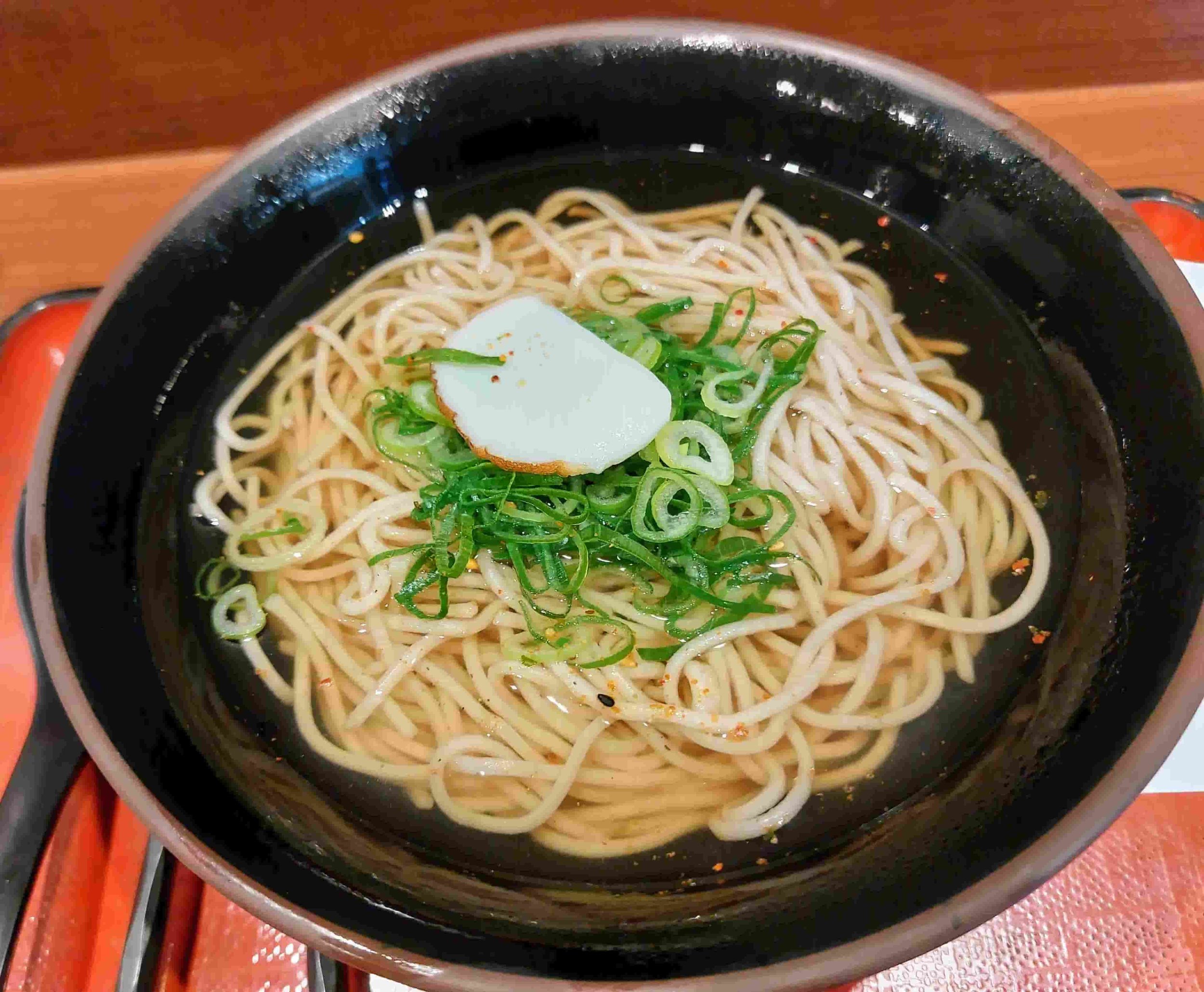 Japanese kake soba noodle soup topped with a piece of fish cake and chopped scallions
