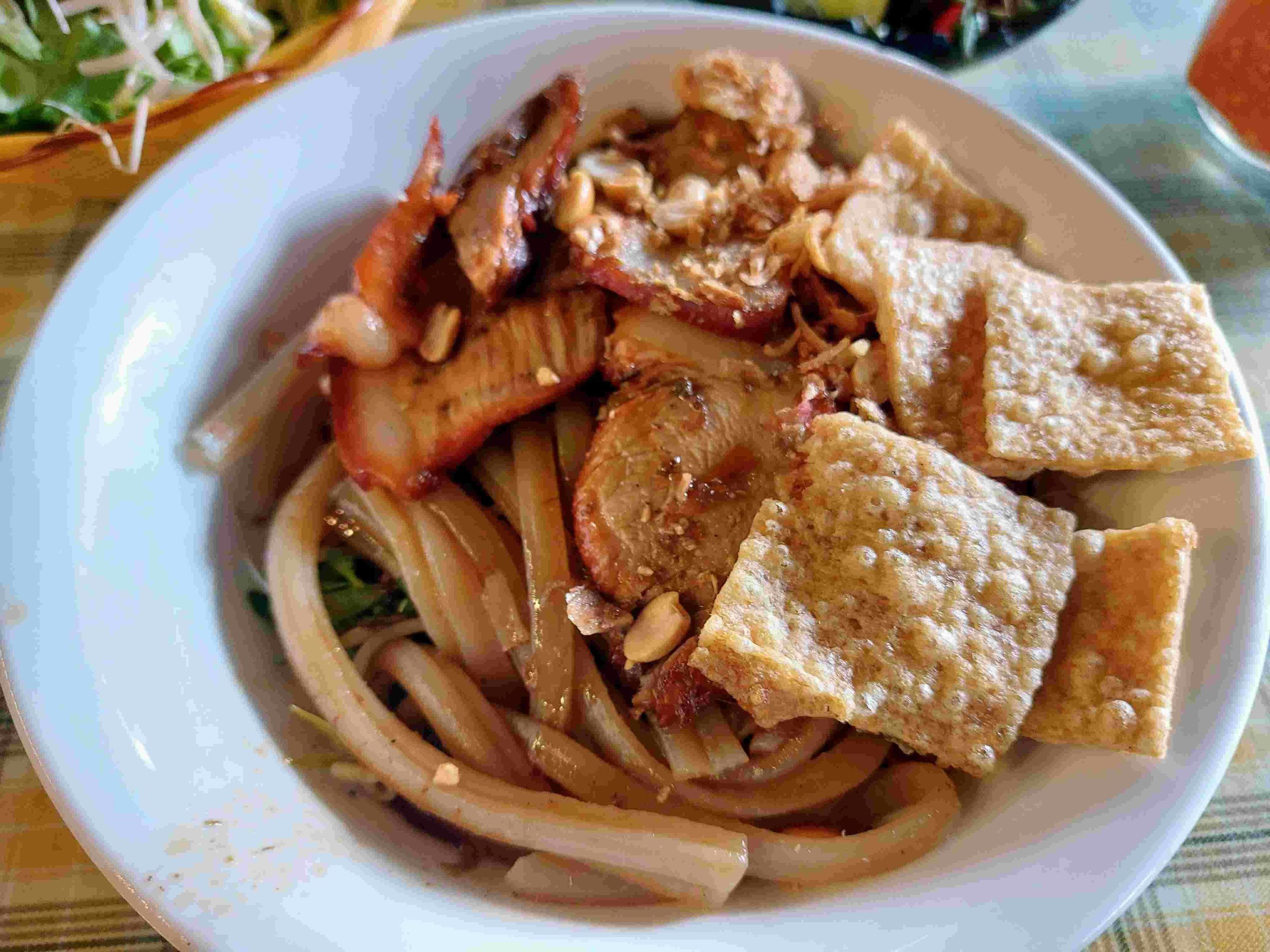 Cao Lau noodles with thick noodles, char siu pork, herbs, and crispy pork crackling