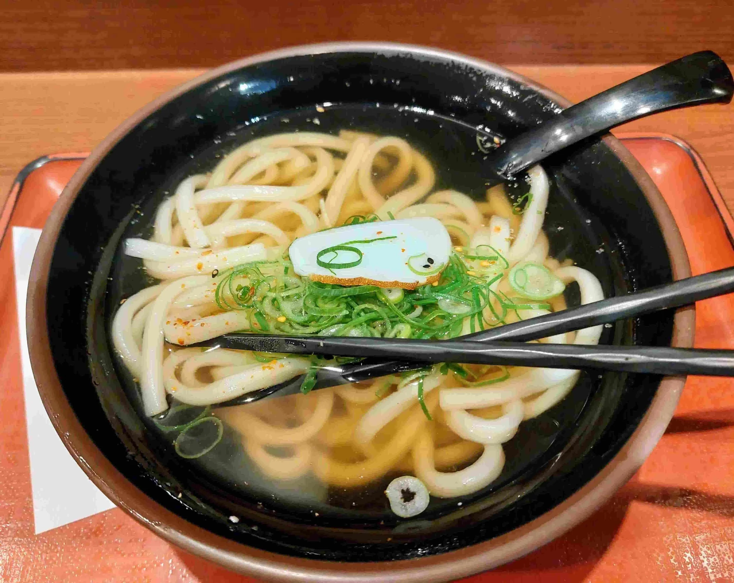 Japanese kake udon noodle soup topped with a piece of fish cake and chopped scallions