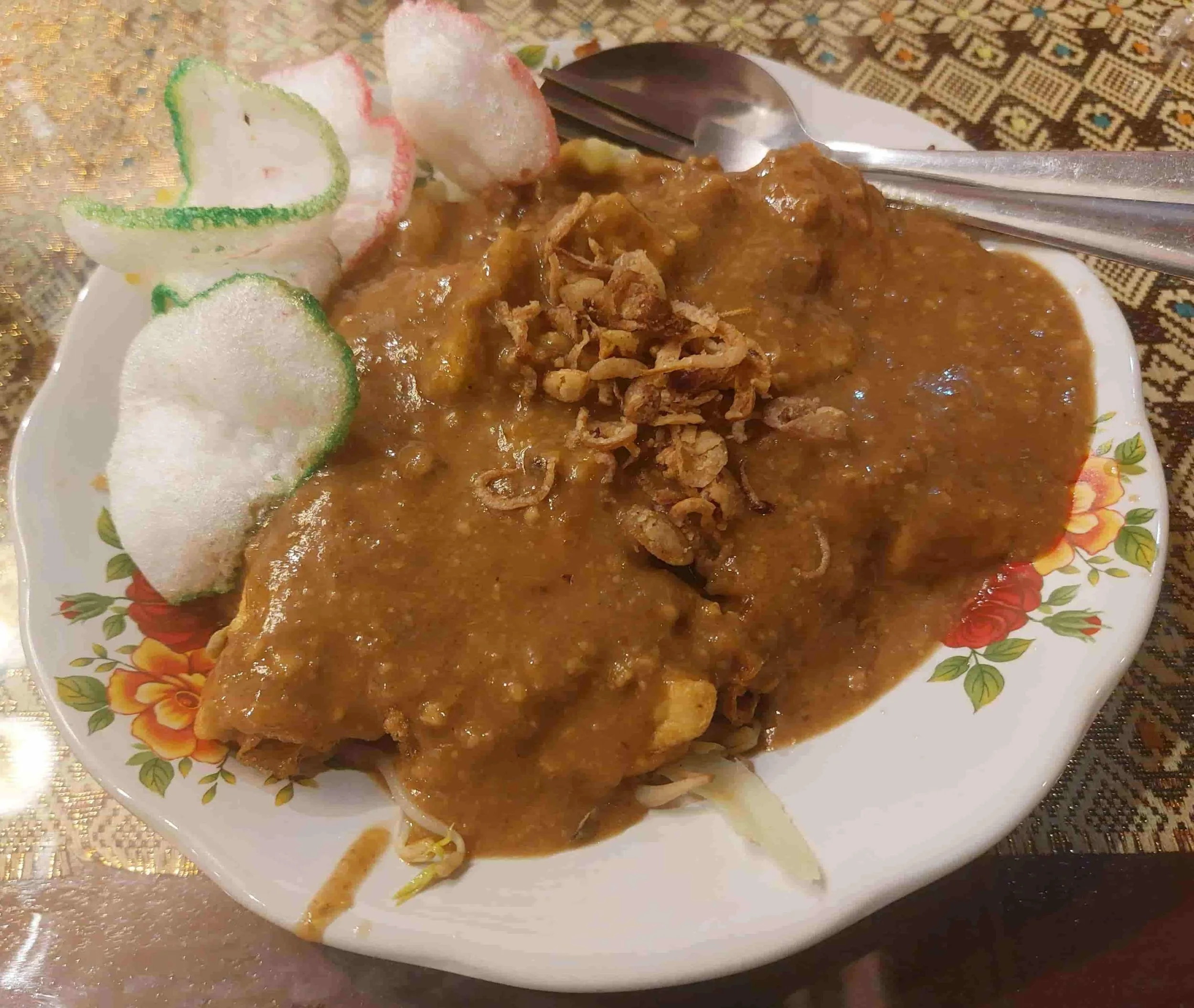 Plate of tahu tek tofu salad topped with peanut sauce, accompanied by crunchy crackers