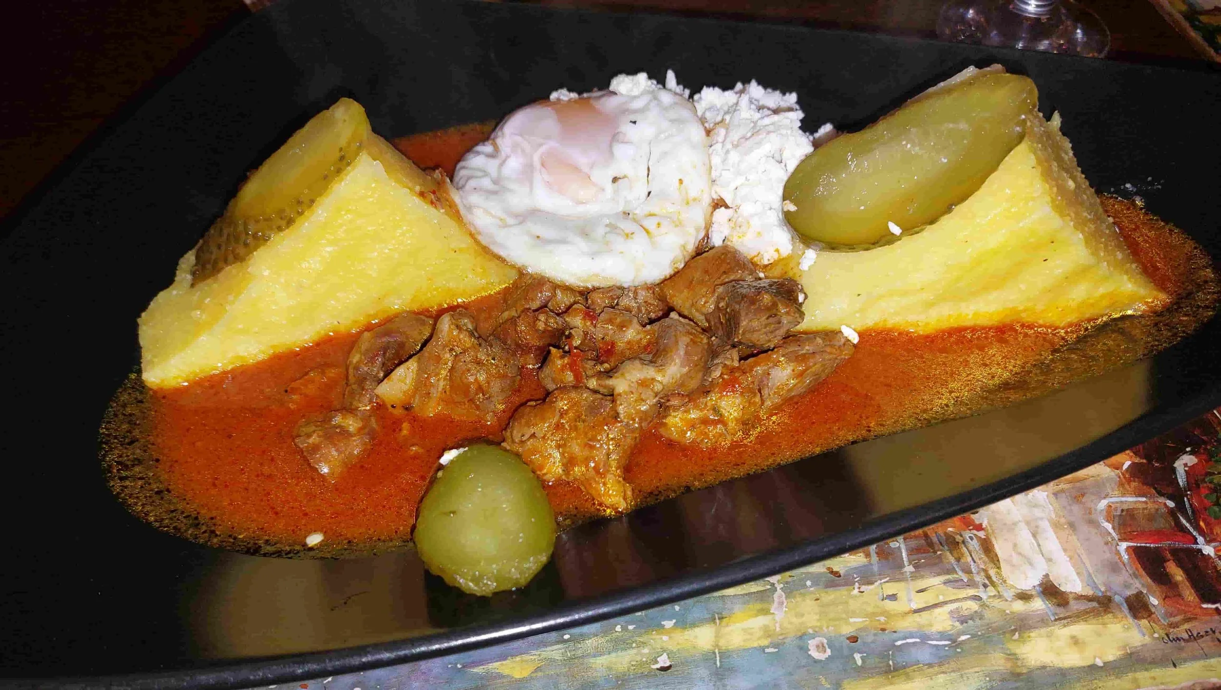 Traditional tochitură Romanian pork stew served with fried egg, mămăligă and pickles