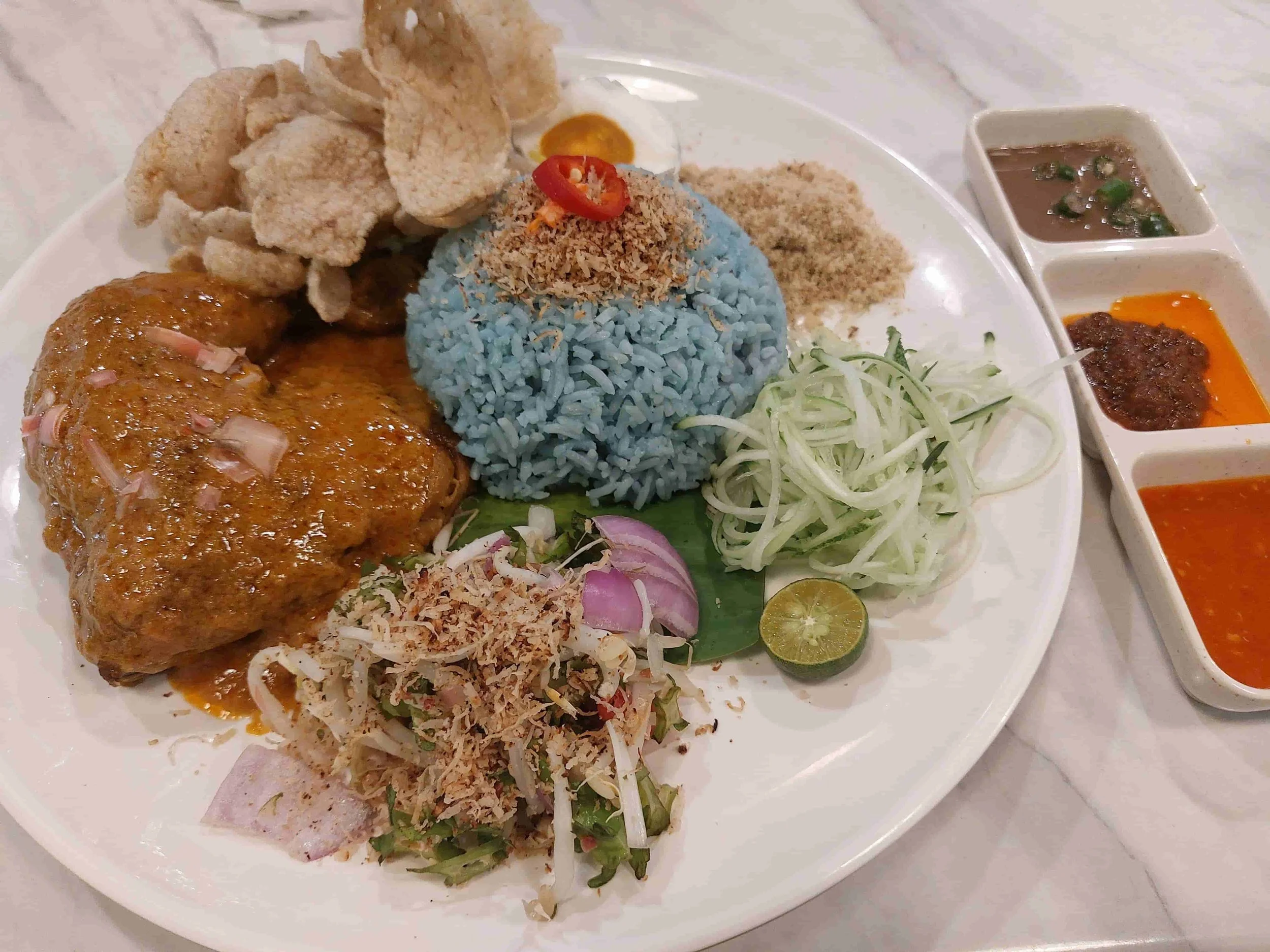 Nasi kerabu – Malaysian blue rice served with chicken, crackers, herbs, and side dishes