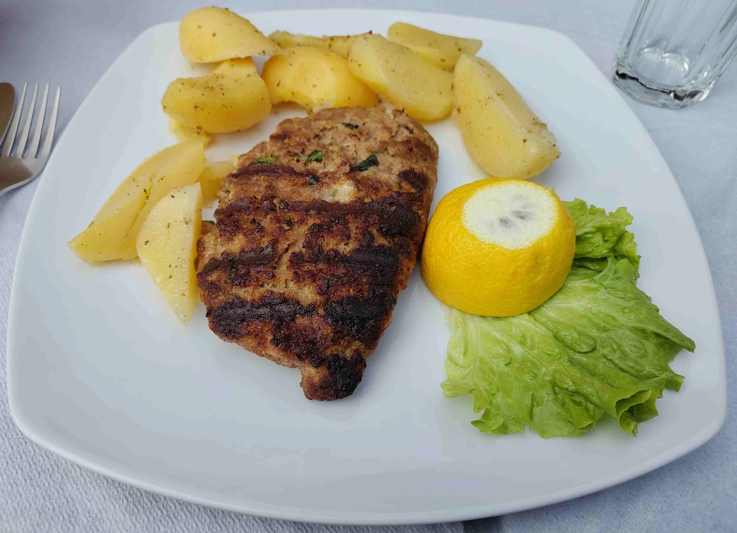Bifteki – Greek minced meat patties served with potatoes, salad, and lemon