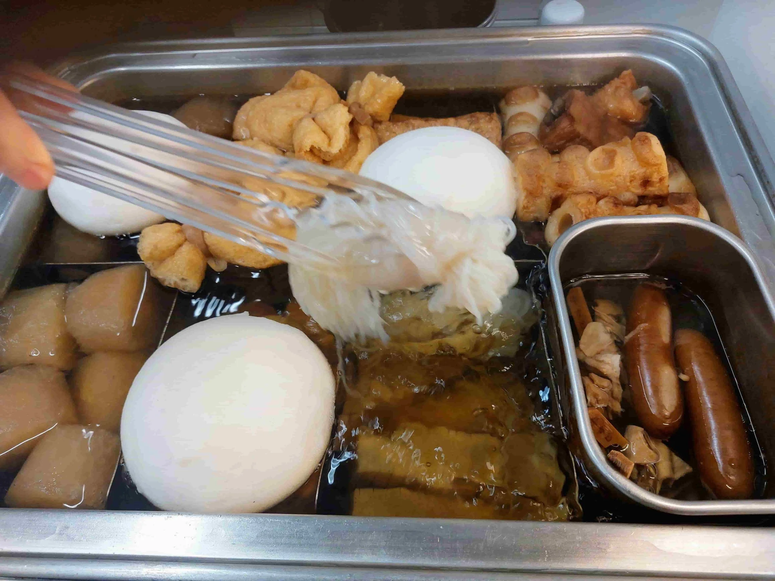 Japanese oden counter displaying a variety of simmered ingredients like daikon, eggs, fish cakes, and tofu