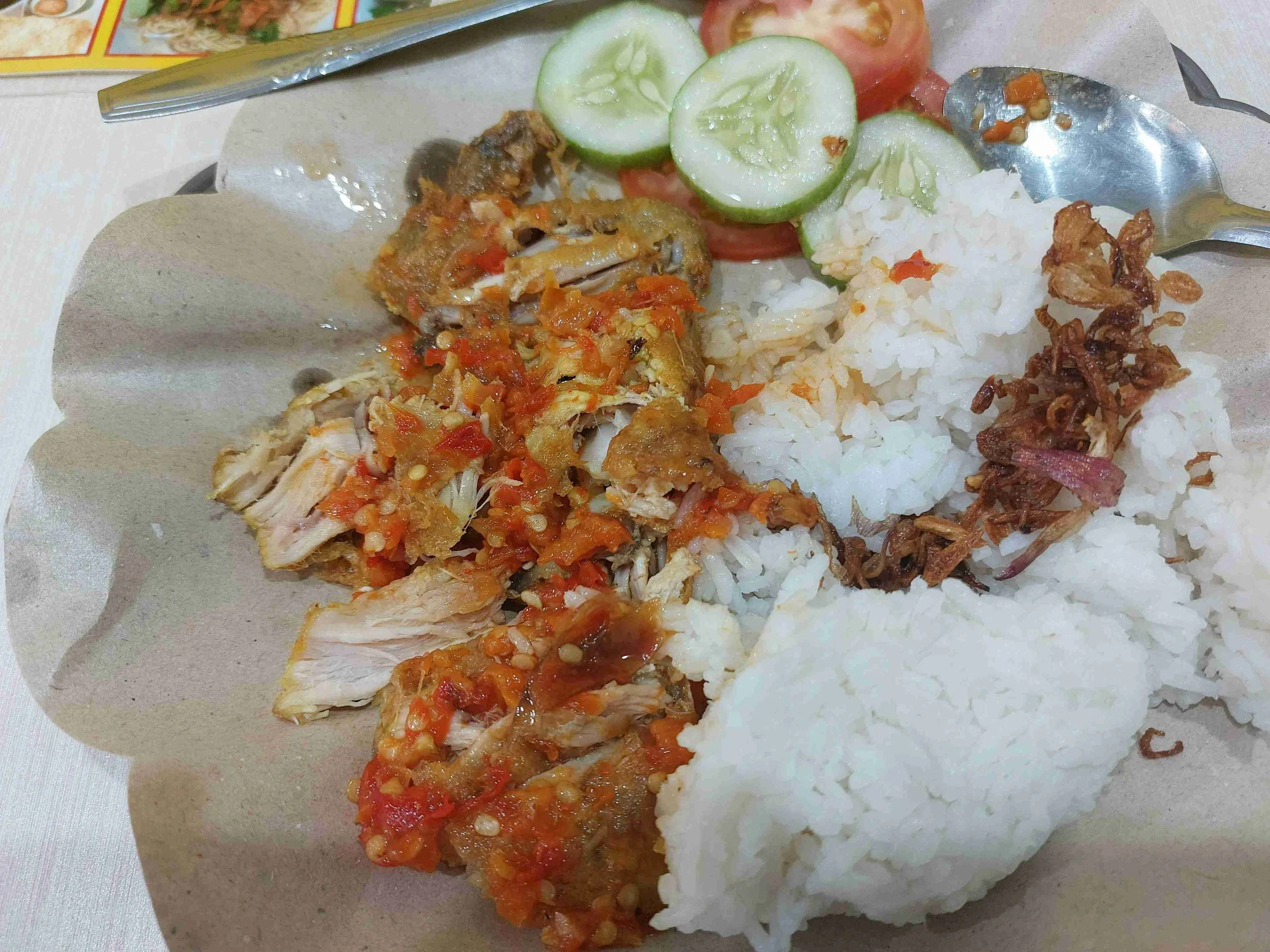 Ayam geprek – smashed Indonesian fried chicken topped with spicy sambal, served with steamed rice, cucumber slices, and tomato wedges