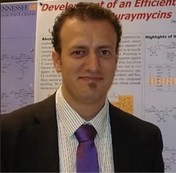 Man in a suit and tie standing in front of research posters at a conference.
