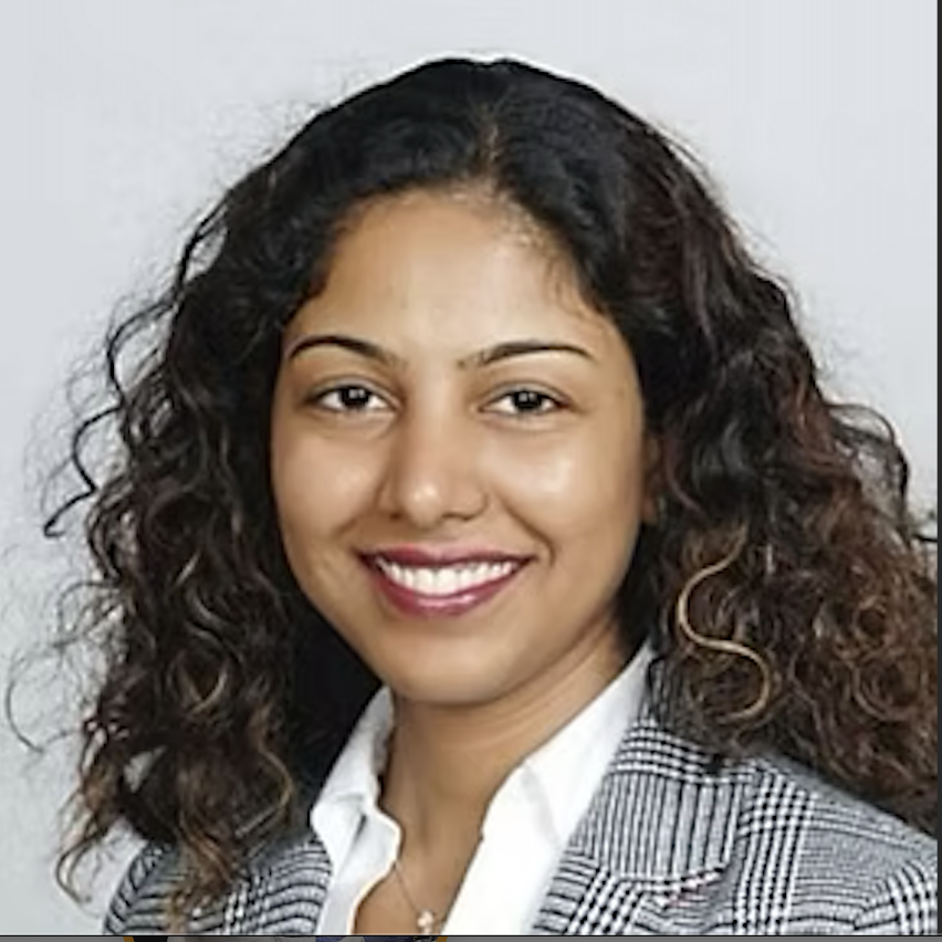 A woman with curly dark hair, wearing a gray checkered blazer and a white shirt, smiling at the camera.