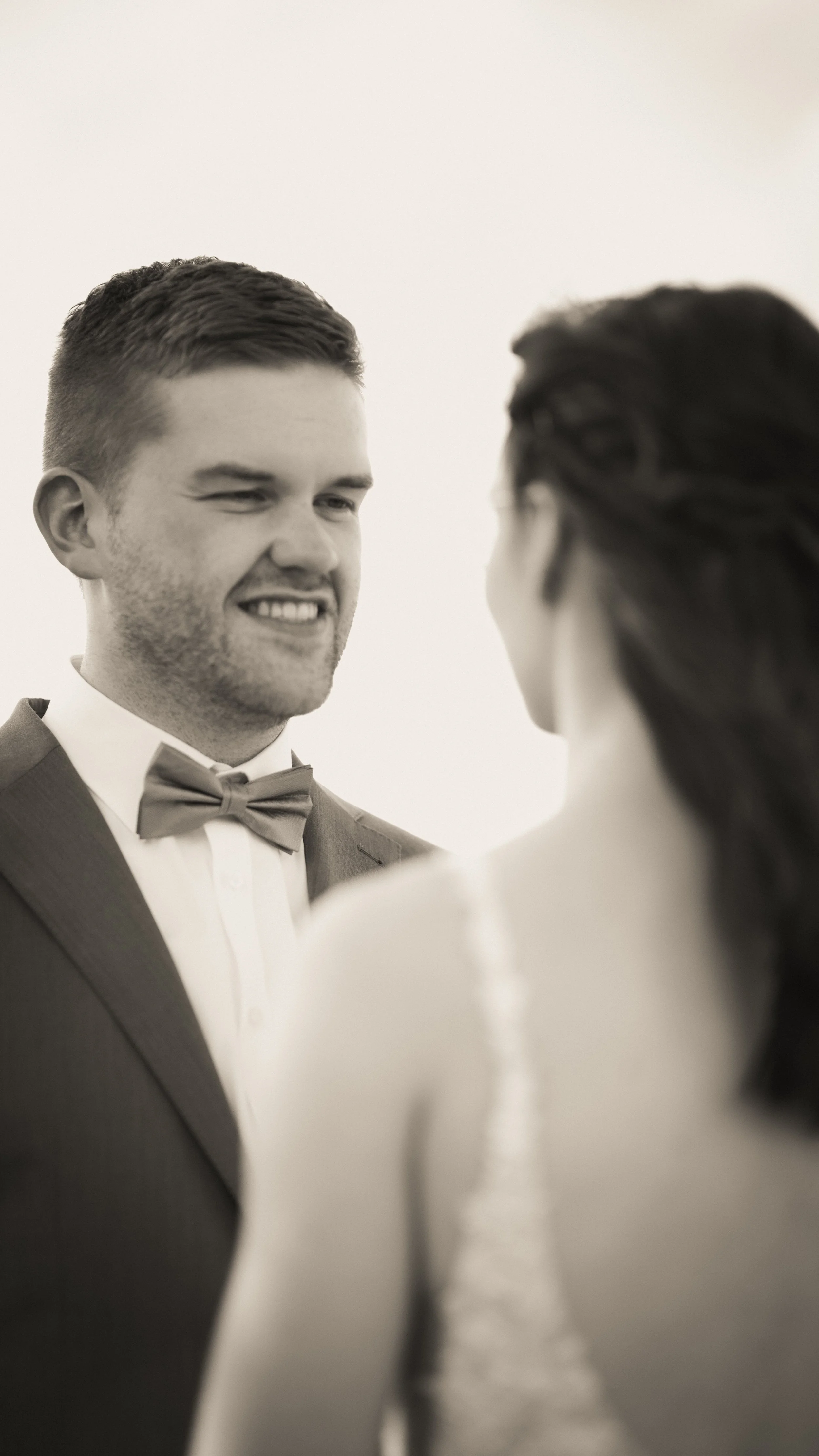 Ein Mann lächelt den Braut an, beide tragen formelle Kleidung, wahrscheinlich während einer Hochzeitszeremonie.