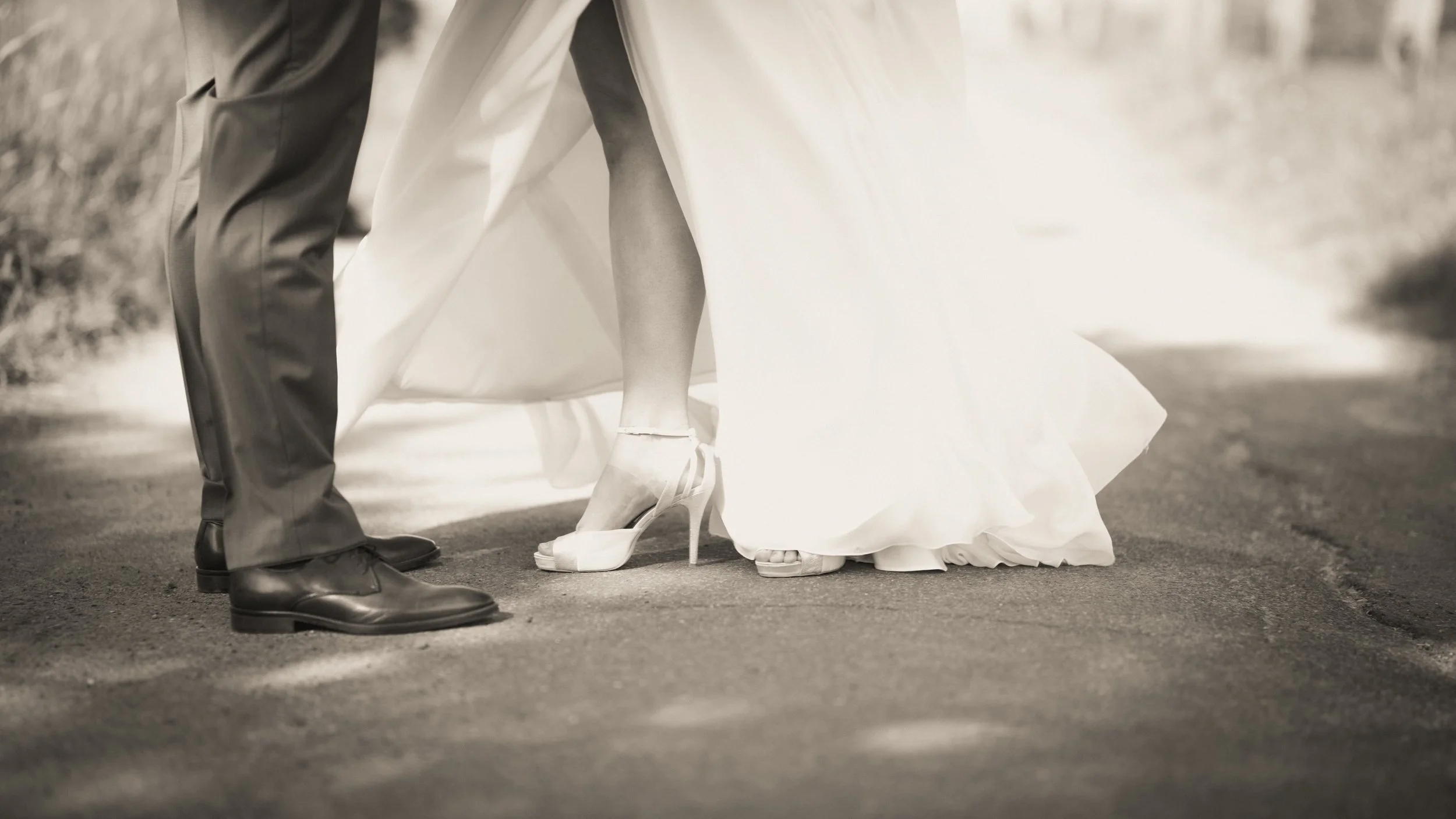 Ein Brautpaar tanzt, nur die Beine und Füße sind sichtbar, die Braut trägt hohe Sandaletten, der Bräutigam trägt schwarze Lederschuhe.