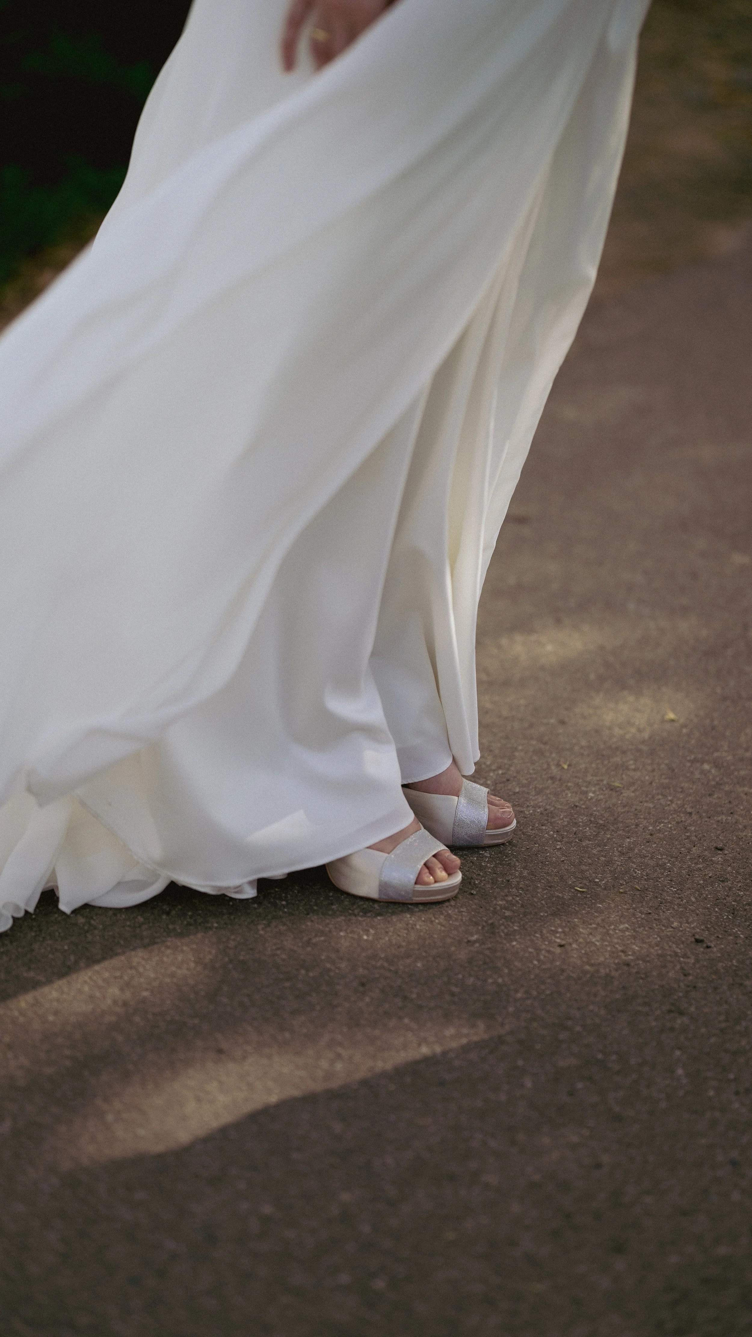 Nahaufnahme eines Brautkleides, das Boden berührt, mit weißen hohen Schuhen, auf einem dunklen Boden.