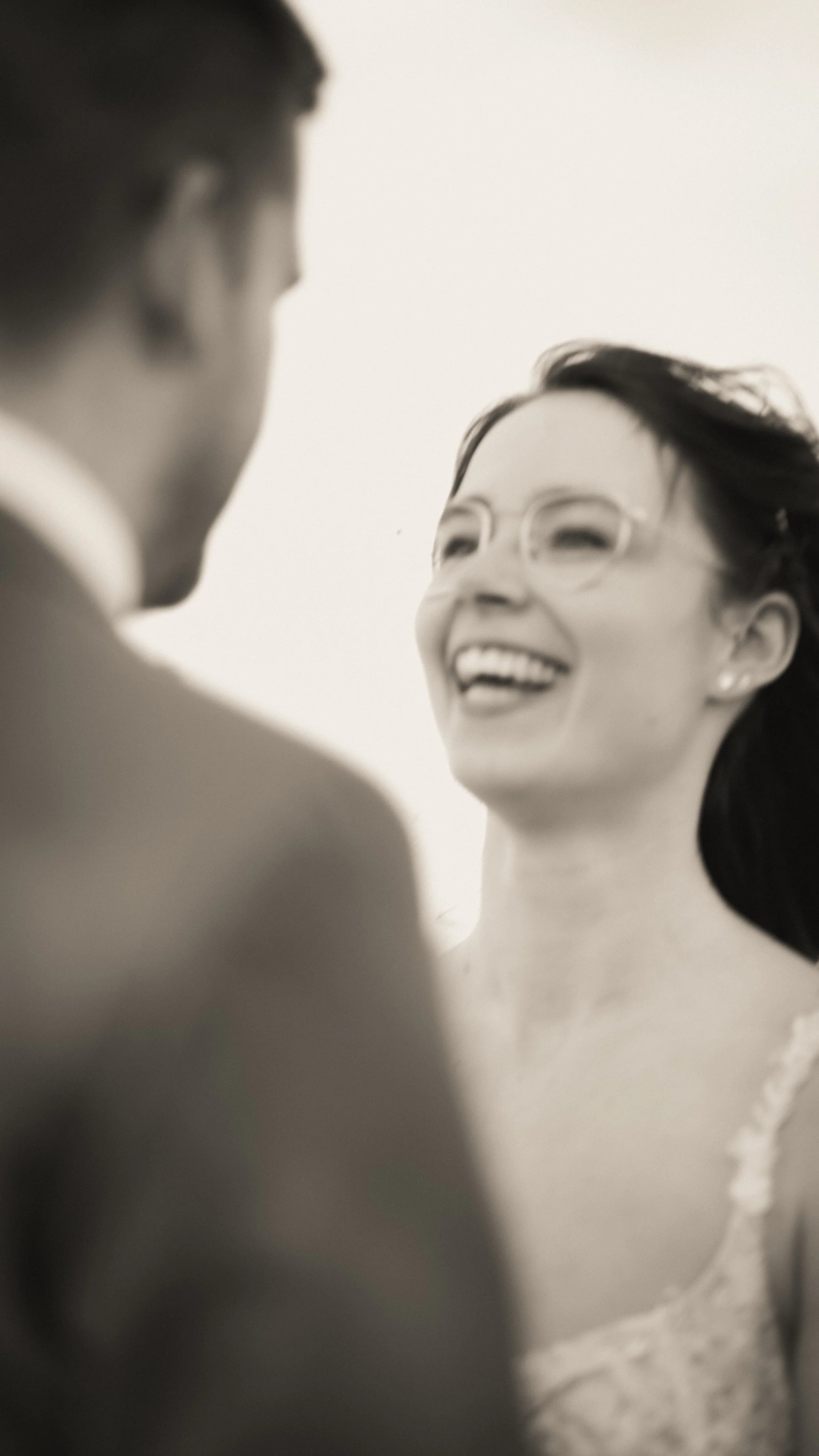 Lächelnde Frau mit Brille, im Vordergrund unscharfe männliche Person, schwarz-weiß