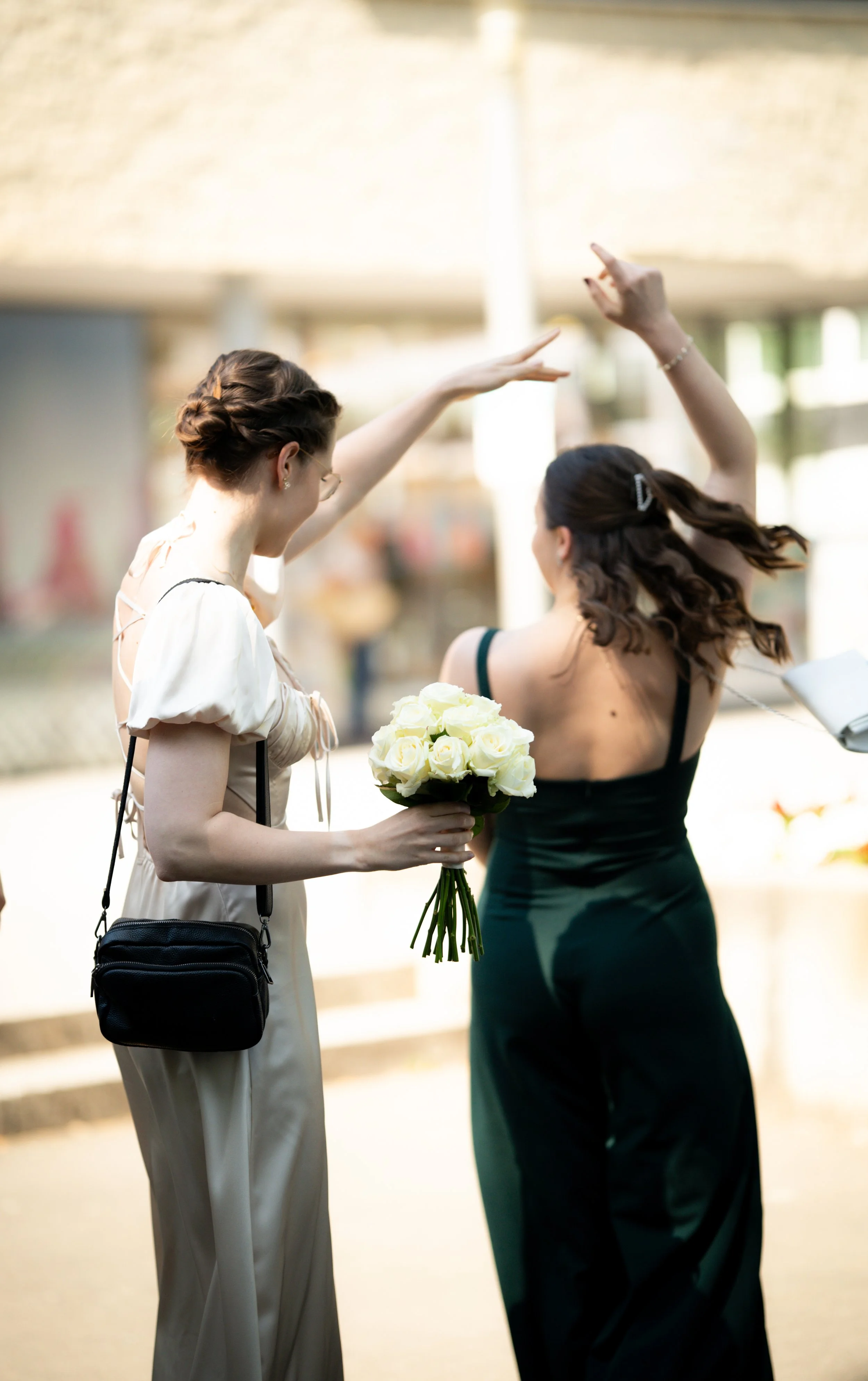 Zwei Frauen, eine mit braunem Haar in einem weißen Kleid und eine mit braunem Haar in einem schwarzen Kleid, tauschen Blumen bei einer Hochzeit.