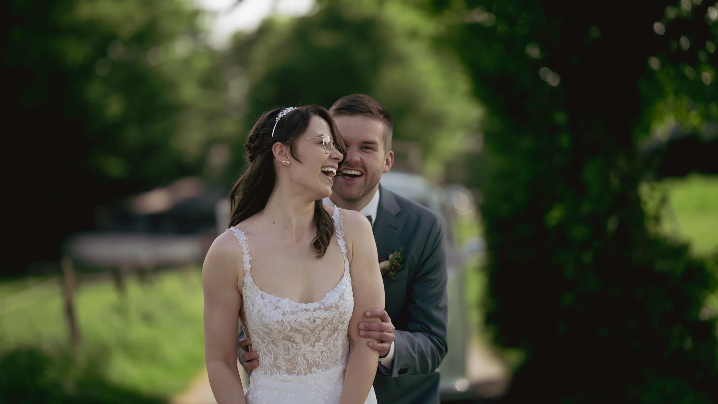 Ein lächelndes Brautpaar bei einer Hochzeit im Freien, umgeben von Bäumen.