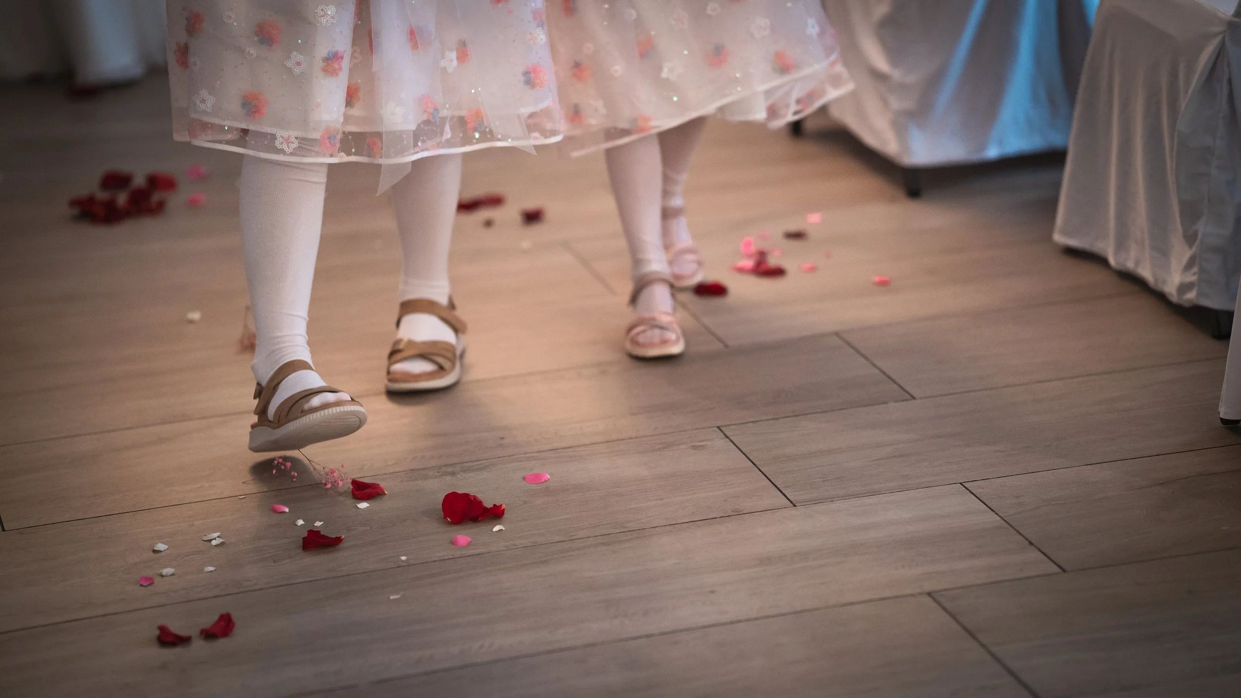 Kinder tanzen auf einem Parkettboden, umgeben von Rosenblättern und Konfetti bei einer Feier.