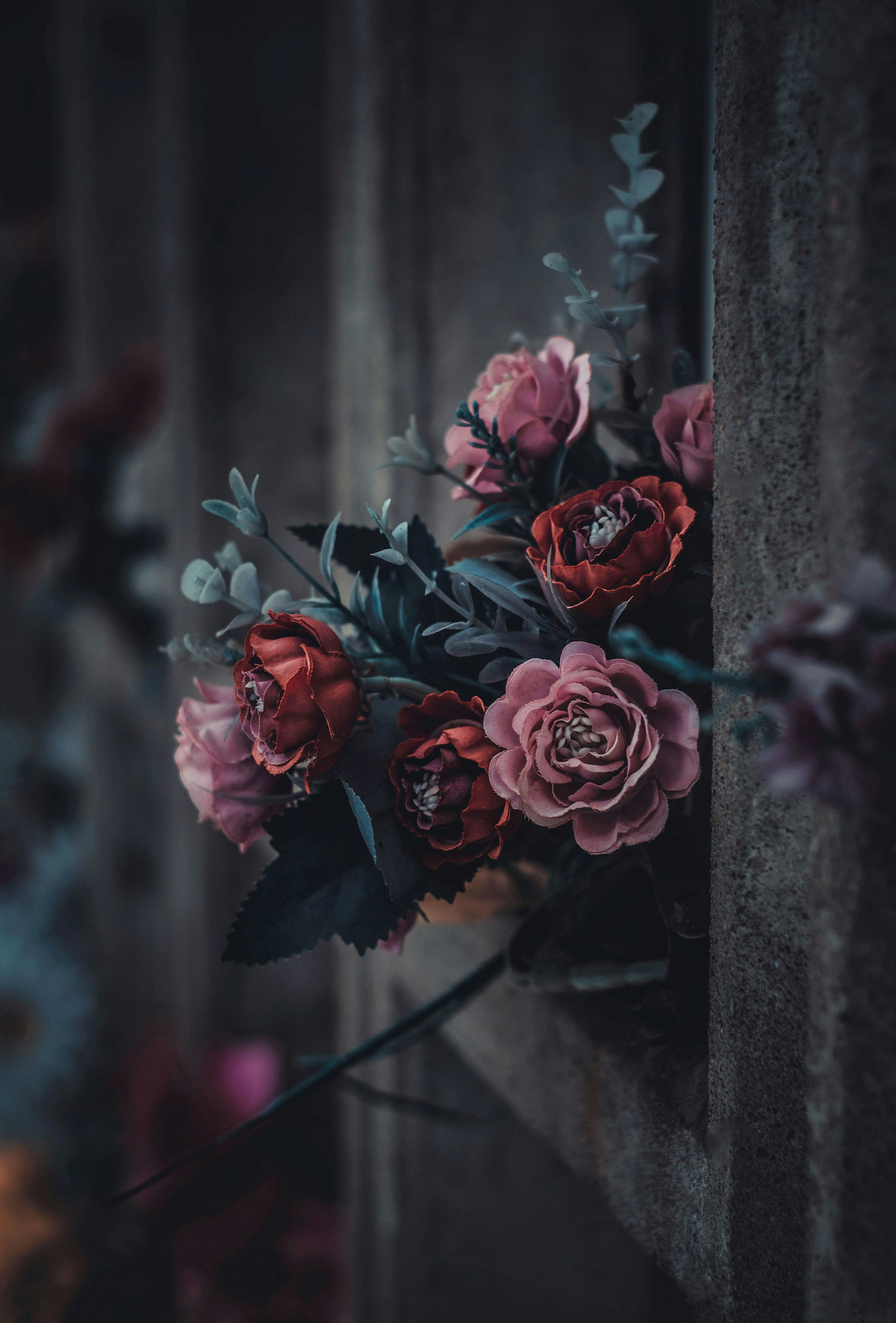 A bouquet of pink and red roses and purple flowers against a brick wall.