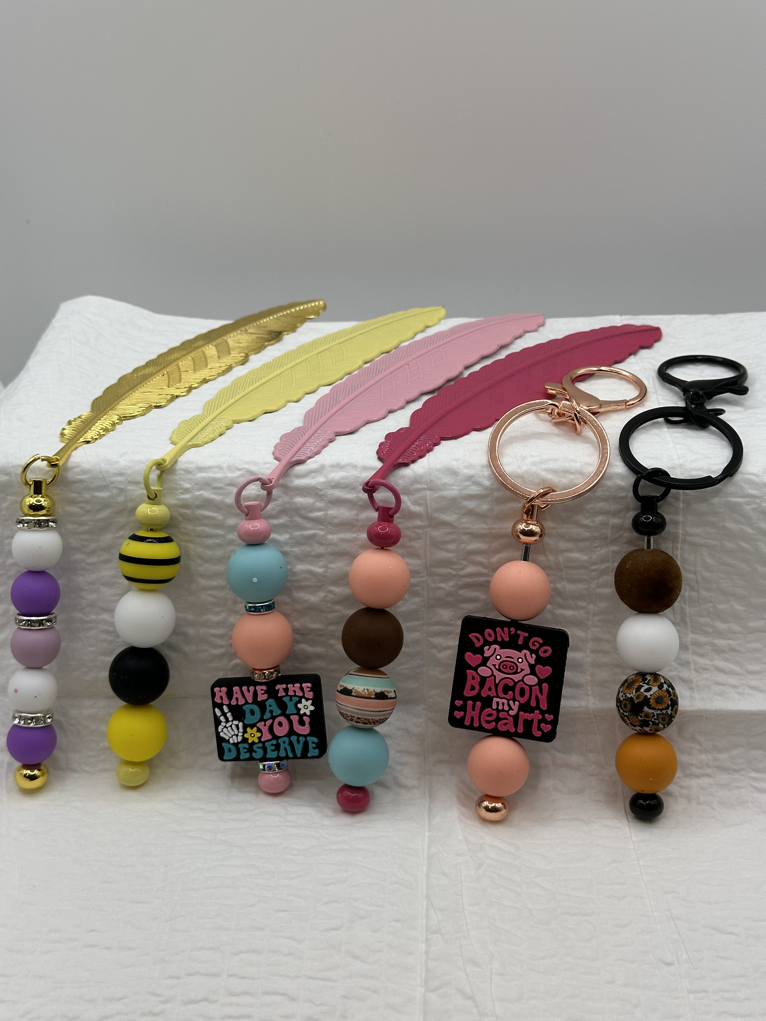 Colorful beaded keychains with feather-shaped straps, displayed on a white surface.