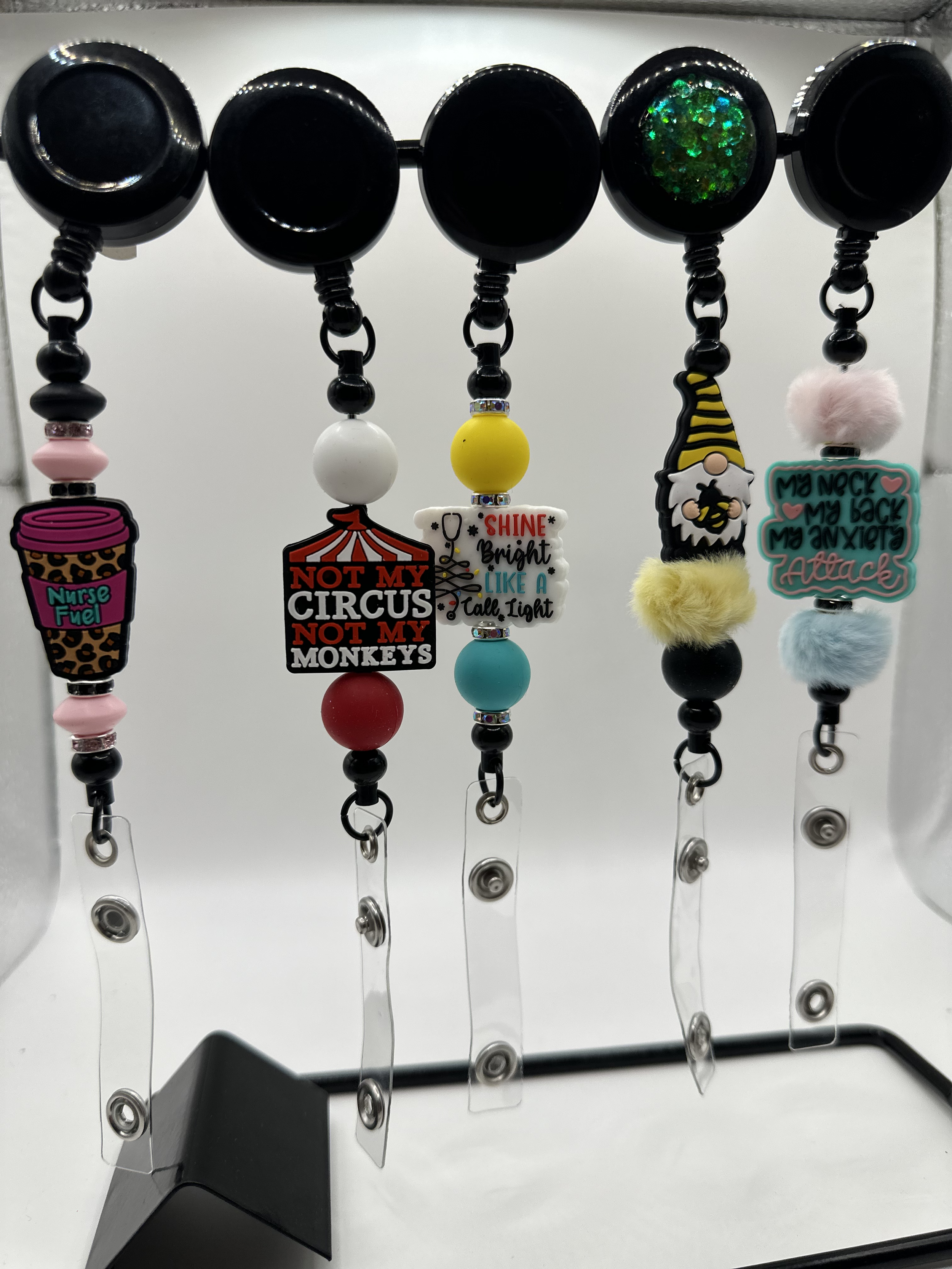 Collection of nurse-themed and humorous badge reels with various colorful beads and charms, displayed on a black stand.