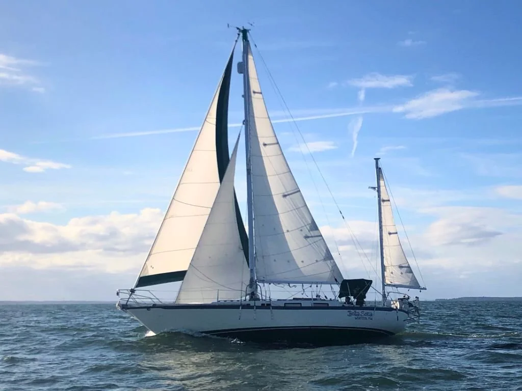 A sailboat with its sails up on the water during daytime, under a blue sky with some clouds.