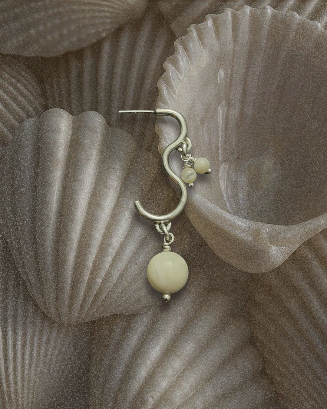 Silver earring with pearl accents on a textured gray seashell background.