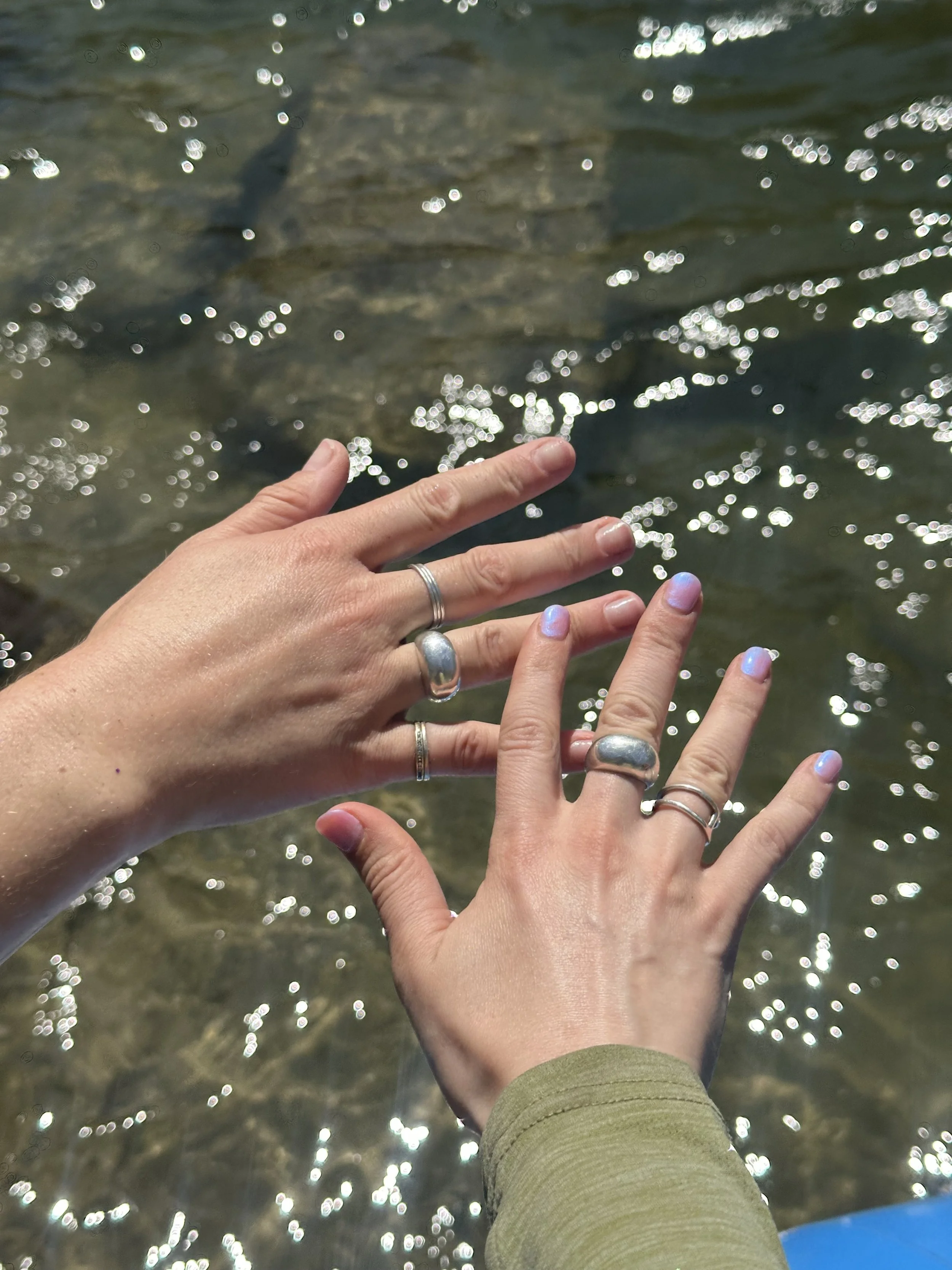two hands wearing handmade sterling silver reflection rings above water