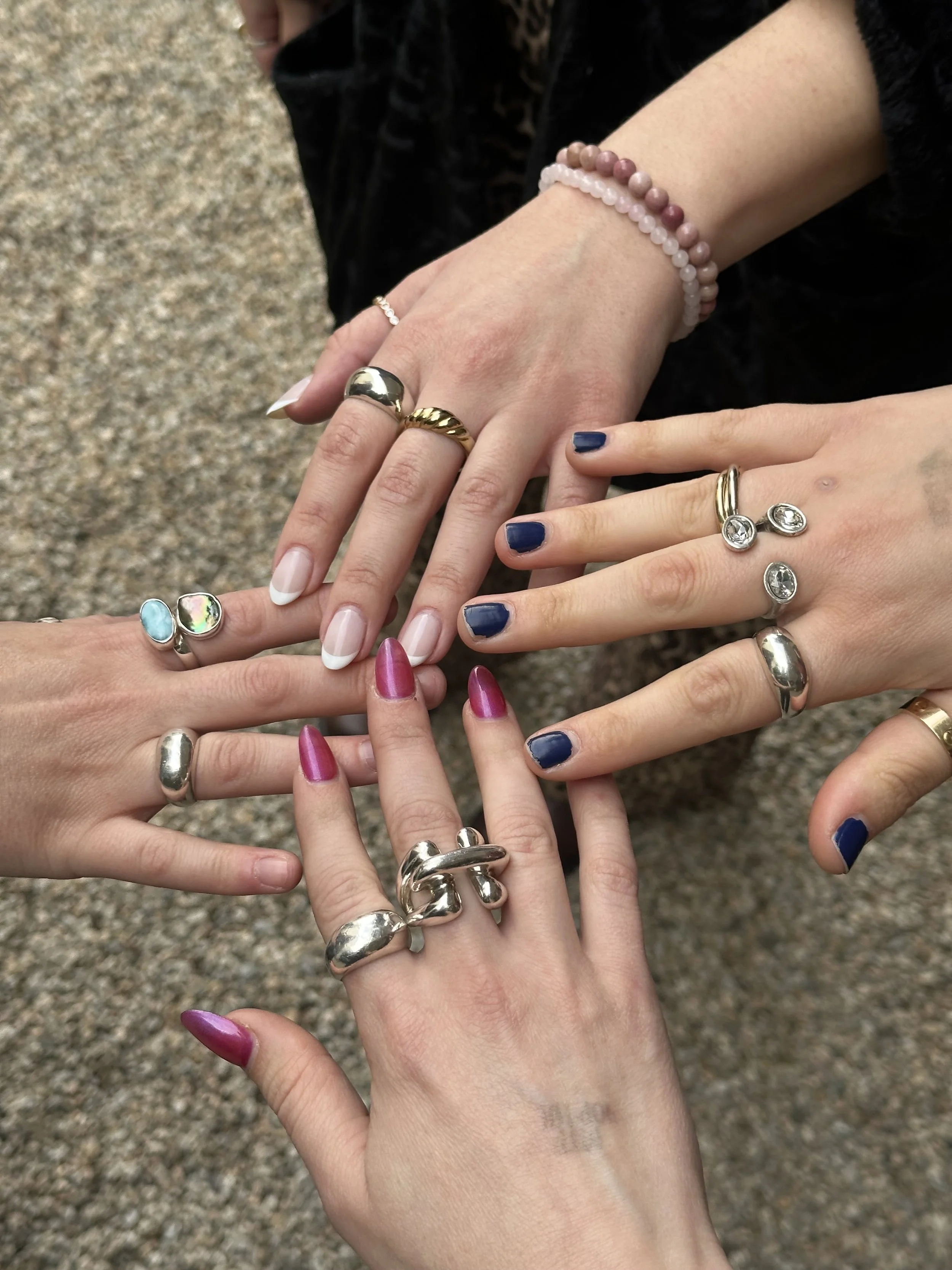 several hands wearing handmade sterling silver rings on the sand