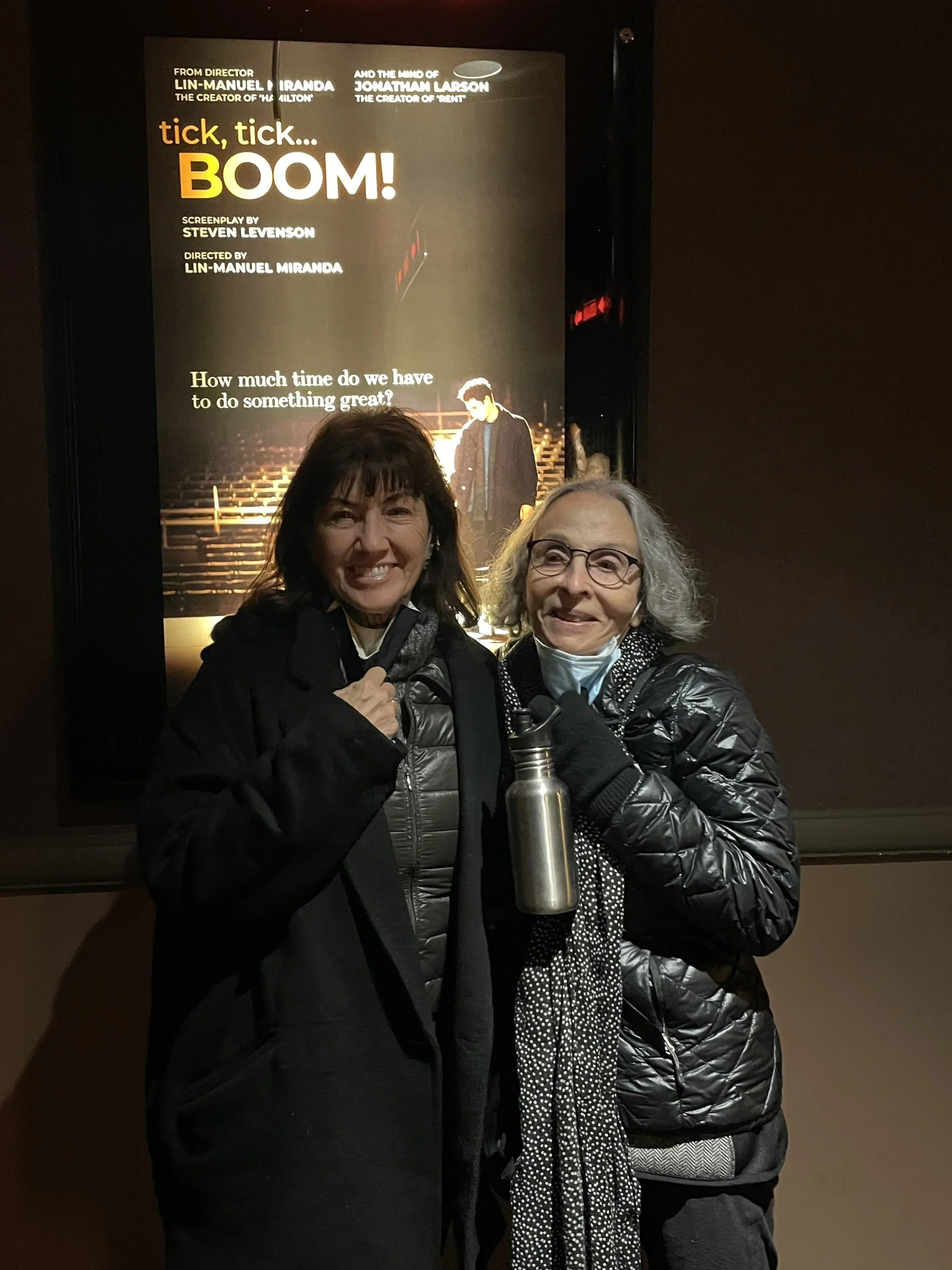 Two women smiling standing in front of a poster