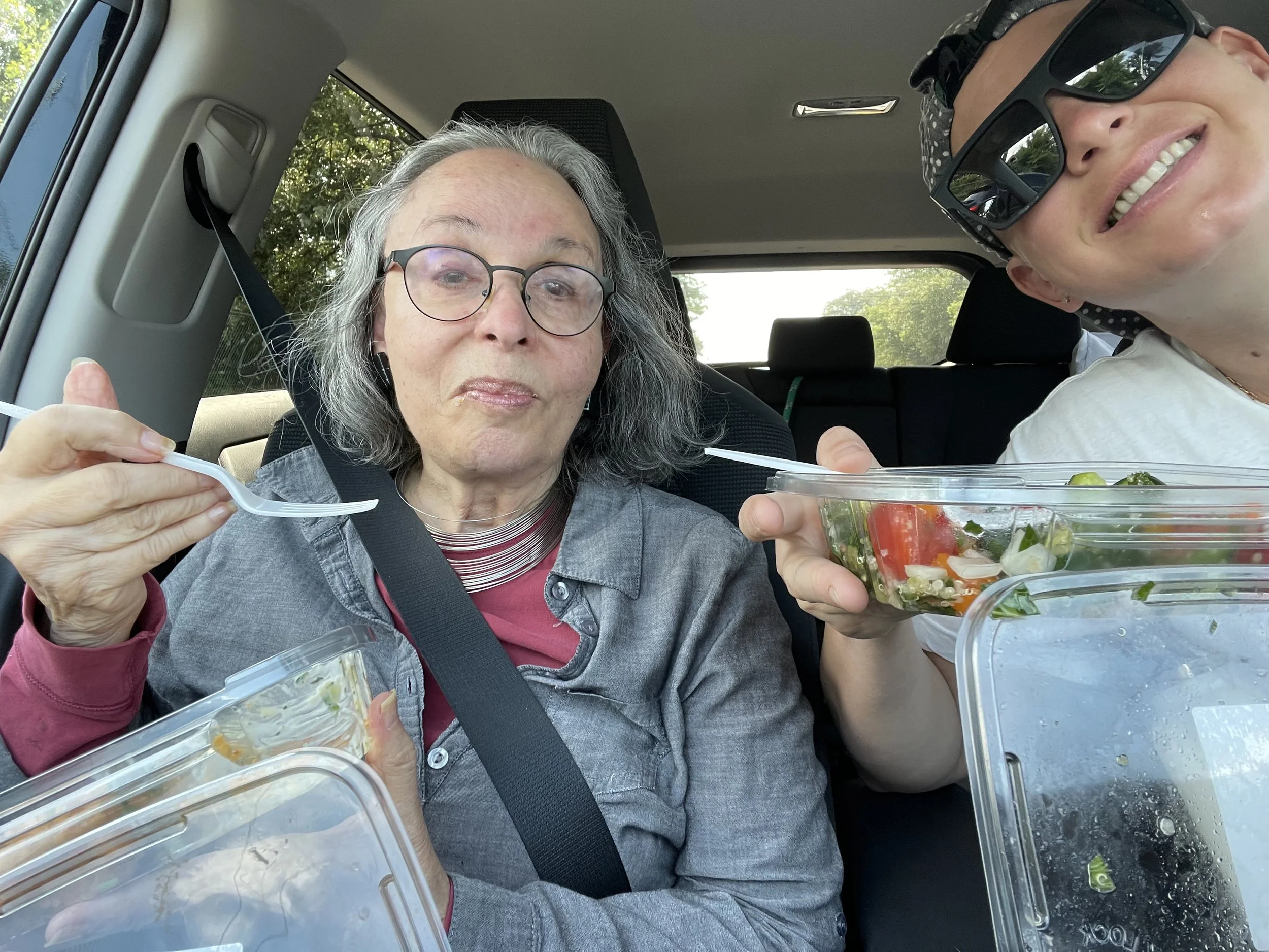 Two women eating in a car together and smiling