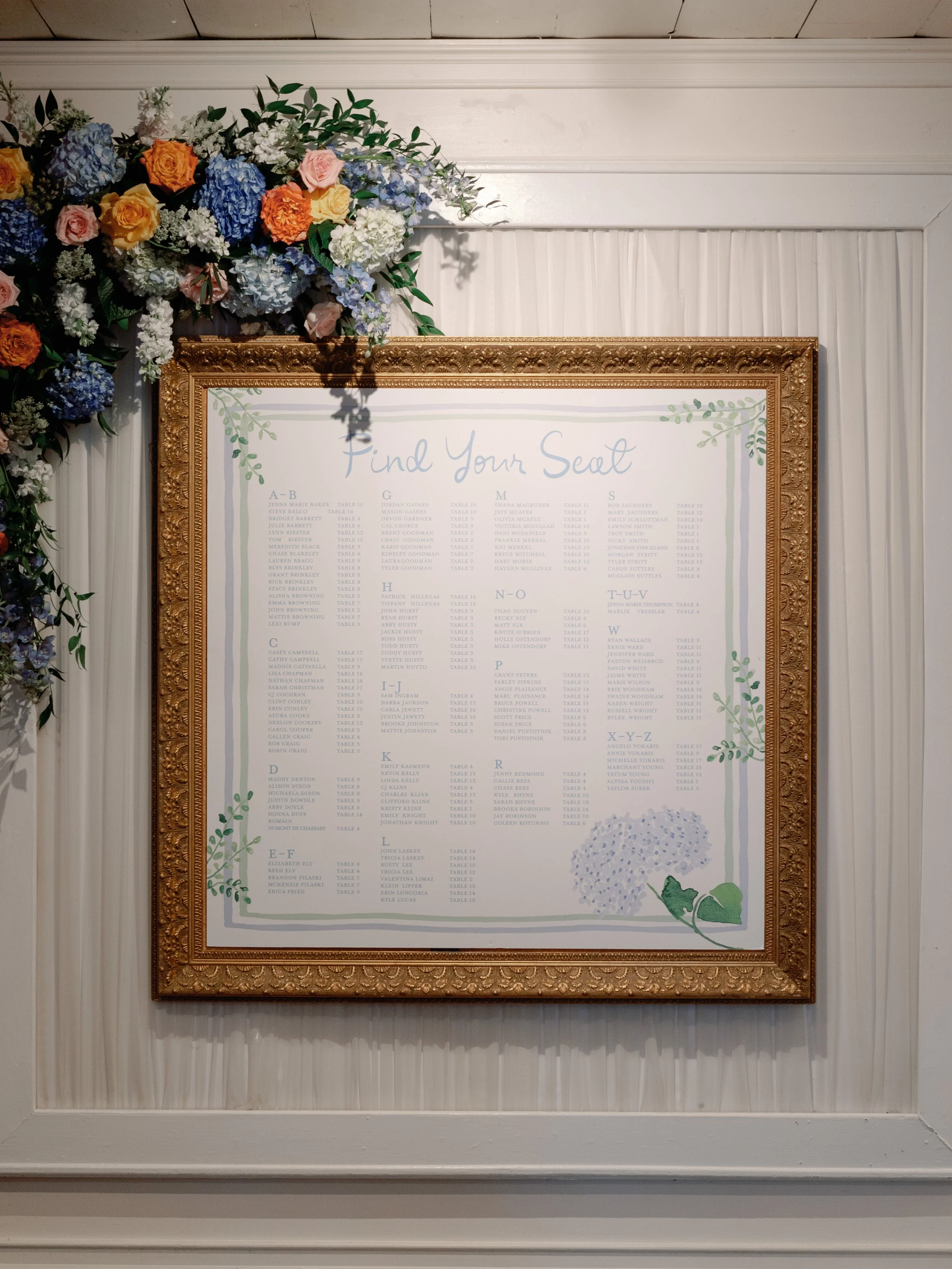 Wedding seating chart titled 'Find Your Seat' with floral decorations in the top left corner and bottom right corner, surrounded by a gold ornate frame.