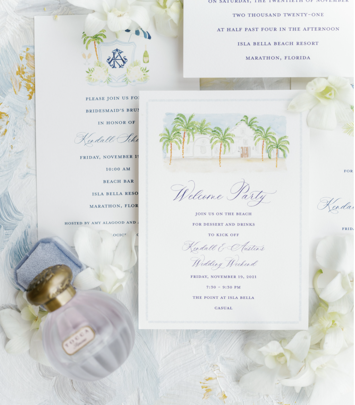 Wedding invitations with tropical theme, decorated with white flowers and a bottle of perfume.