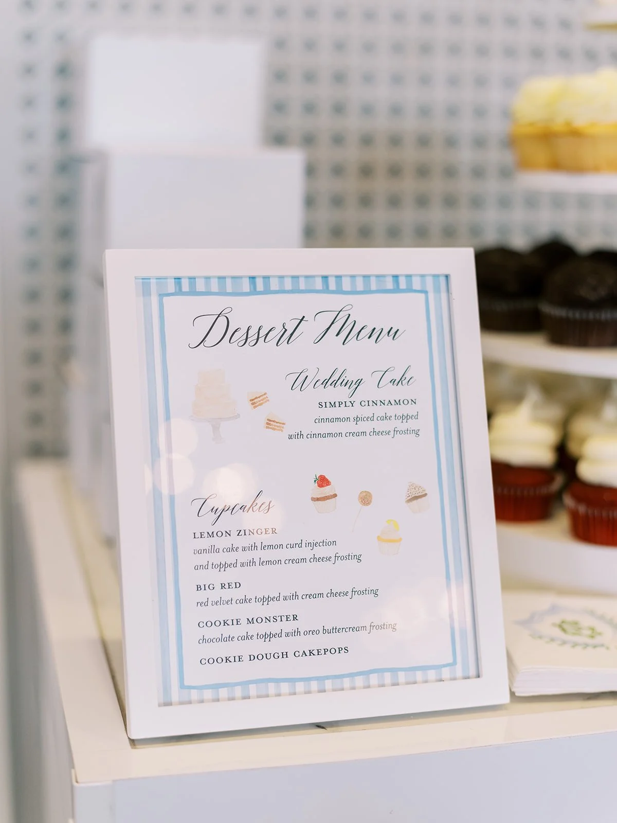 Dessert menu displaying wedding cake and cupcake options, including Simply Cinnamon cake, Lemon Zinger cupcake, Big Red cupcake, Cookie Monster cupcake, and Cookie Dough Cakepops, with cupcakes in the background.