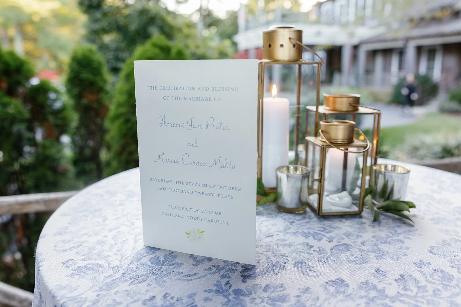 Wedding invitation on a white tablecloth with glass and gold lanterns, and candles outdoors