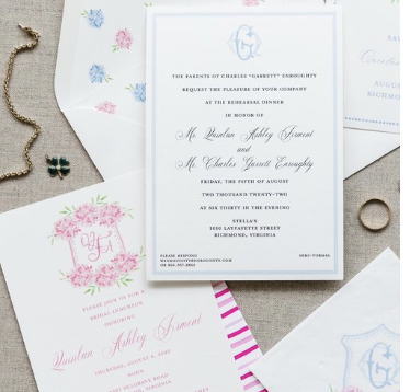Wedding invitation for Dulan Ashley Fament and Charles Garrett Earp. The invitation includes event details and is surrounded by floral and decorative stationery, a small key, and a ring on a textured surface.