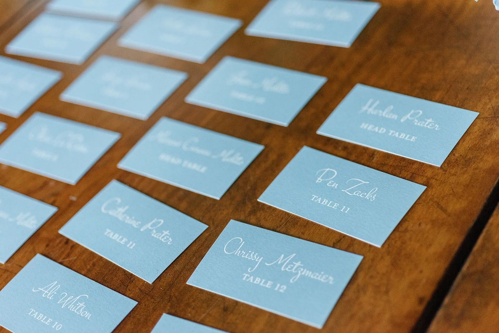 Table name cards in light blue with white cursive text for a wedding or event, placed on a wooden table.