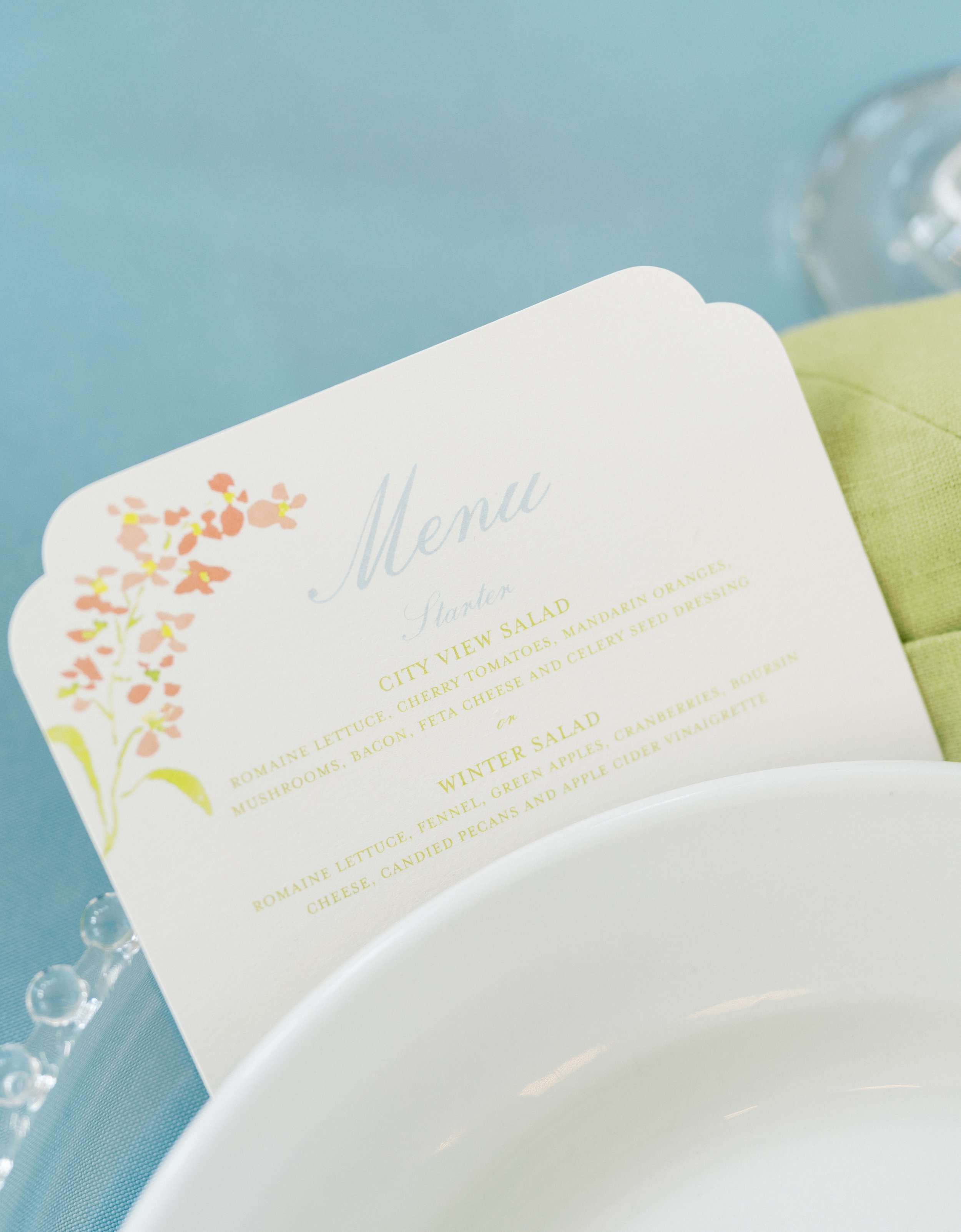 A menu card displaying salad options placed on a white plate with a green napkin and a glass of water in the background.