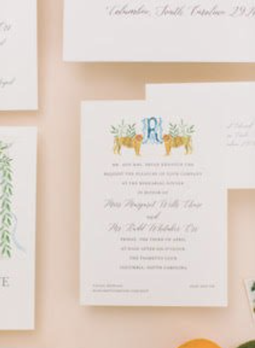 Invitation card with greenery and two tigers flanking a large blue letter 'R' in the center