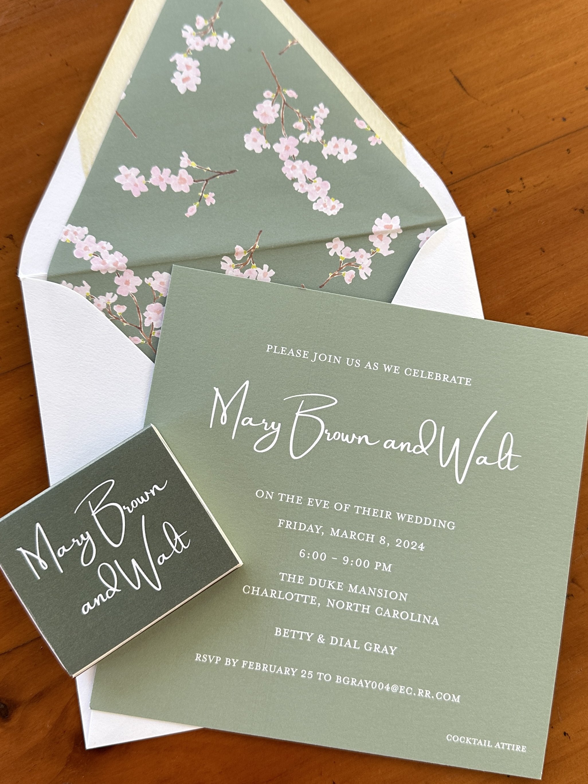 Wedding invitation and RSVP card with cherry blossom design inside a white envelope on a wooden surface.