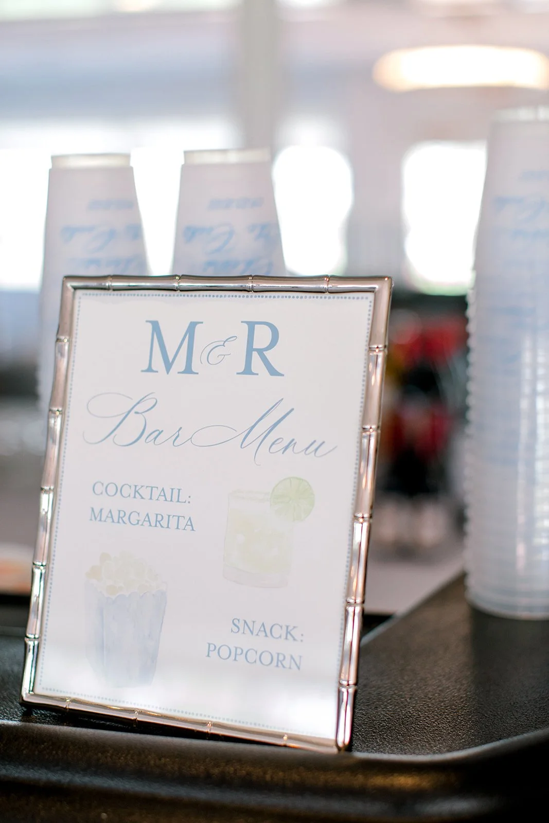 Wedding bar menu sign with cocktail and snack options, surrounded by stacked cups.