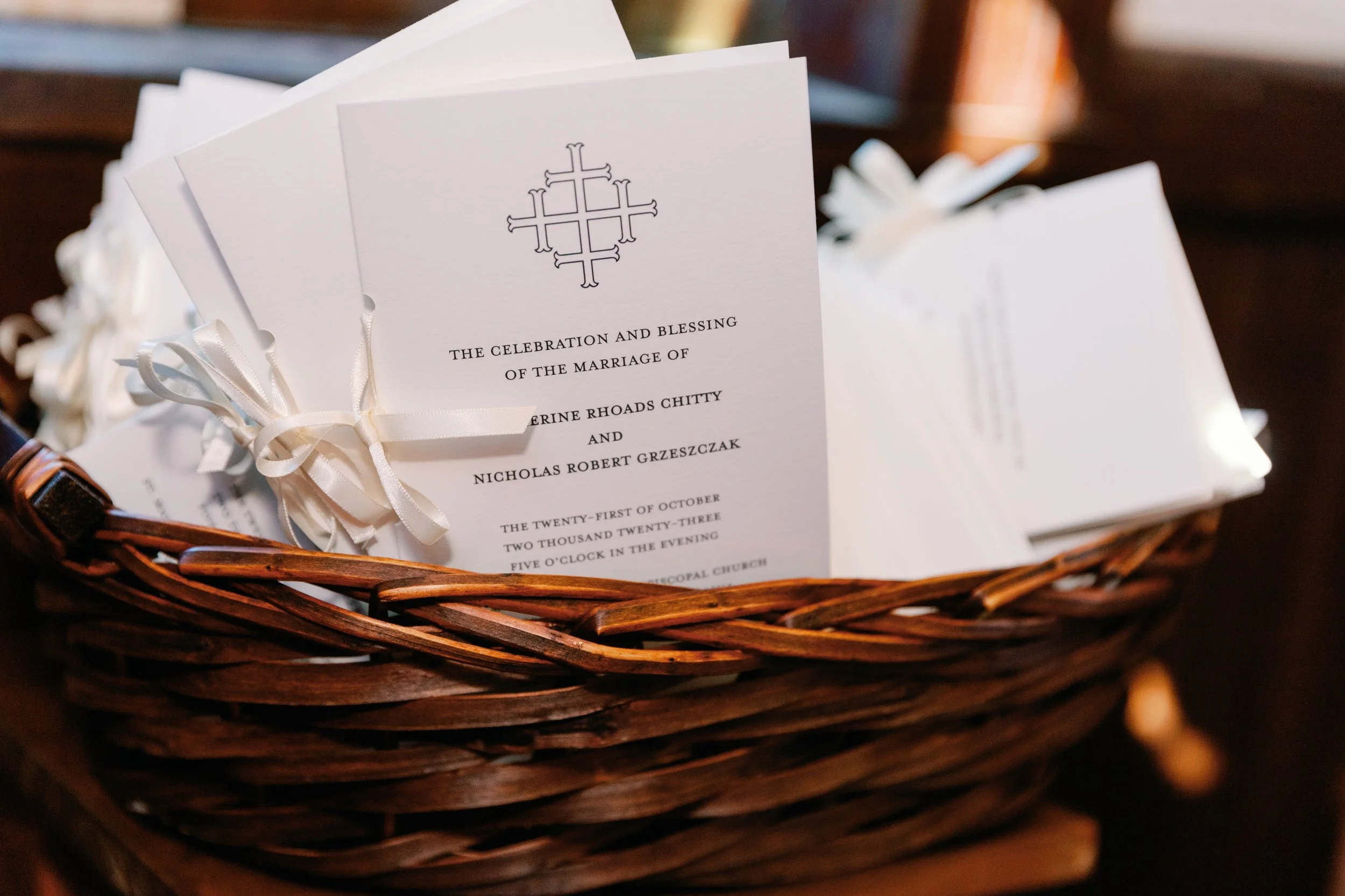 Wedding invitation cards with white ribbons in a woven basket.