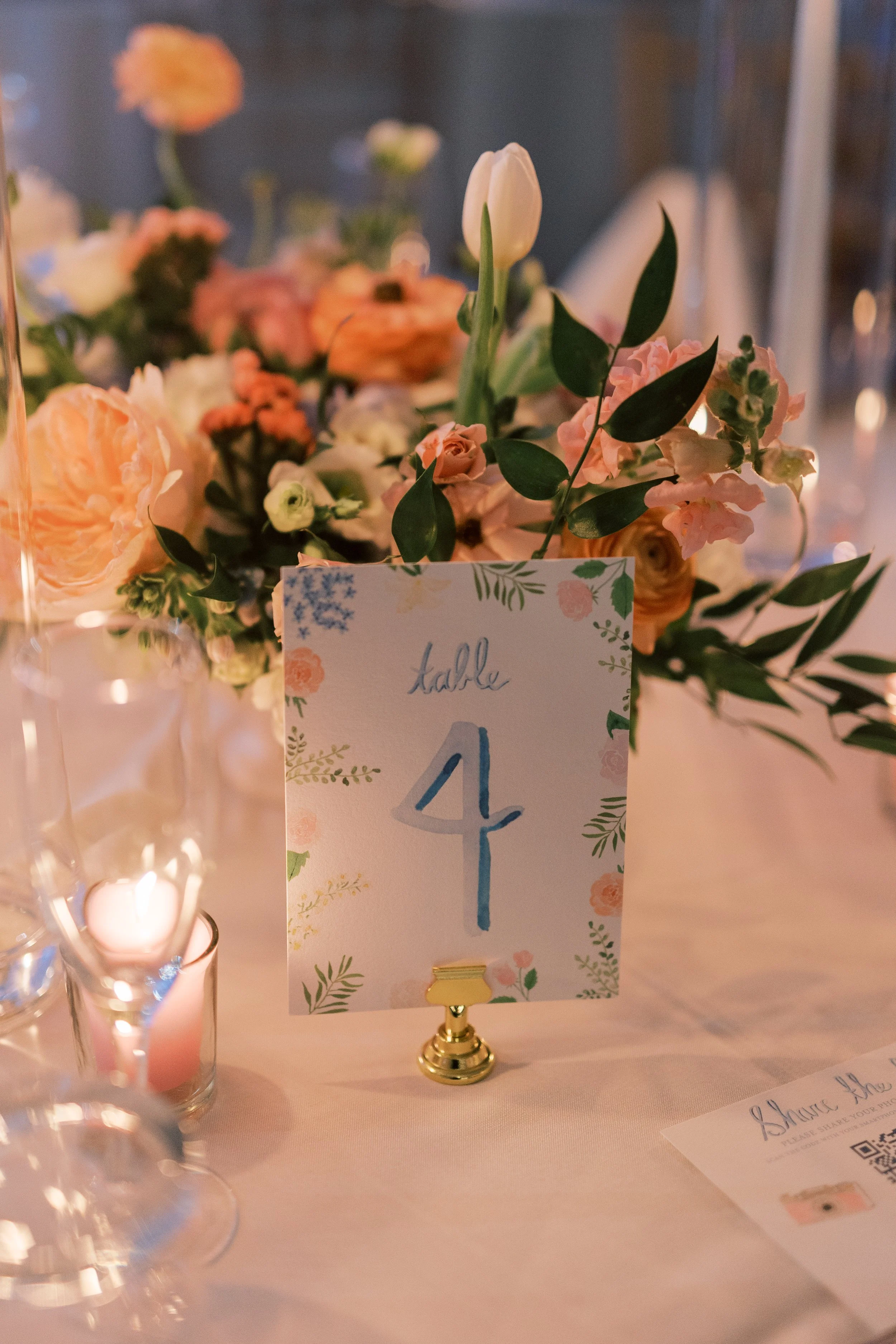 Table number 4 sign on a table decorated with flowers and candles at a wedding reception or formal event.