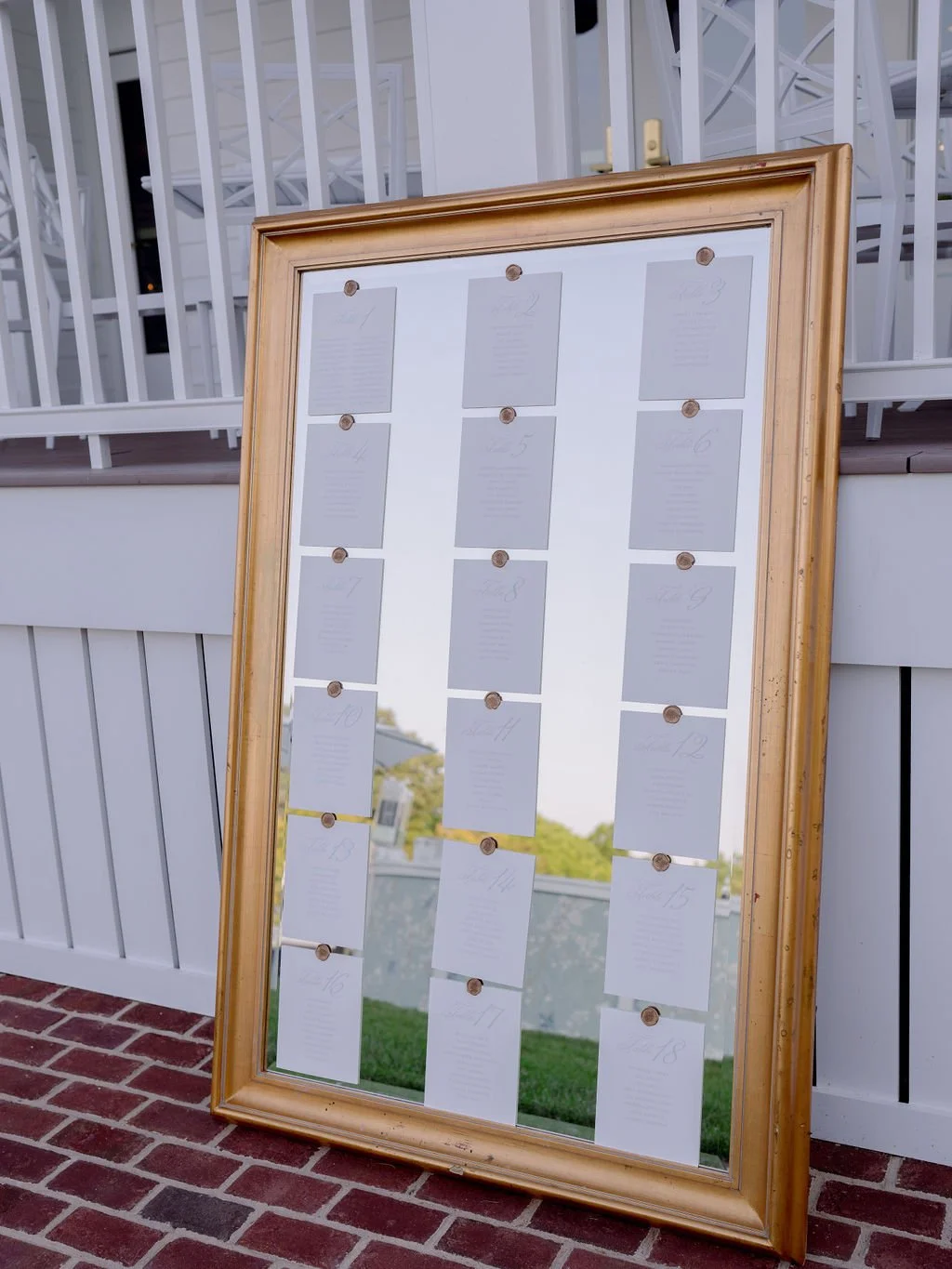 Large mirror with a gold frame displaying seating arrangements for a wedding or event, with numbered cards in a grid pattern.