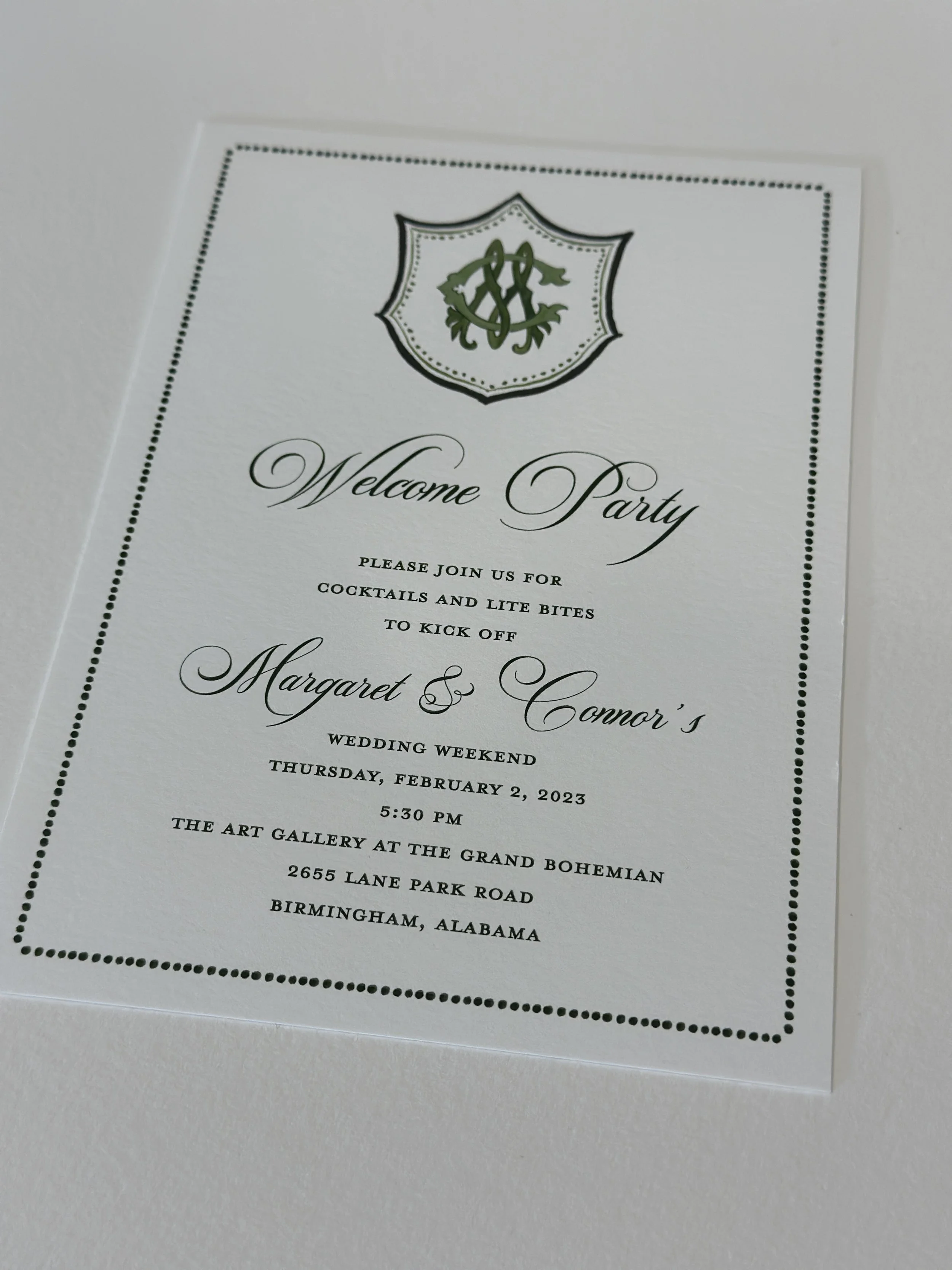 Invitation for a wedding welcome party with elegant script, featuring a monogram crest at the top, black dotted border, and details about the event on a white background.
