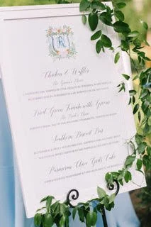 A wedding invitation with elegant floral design, featuring green leaves around the edges, and text in a stylish font.